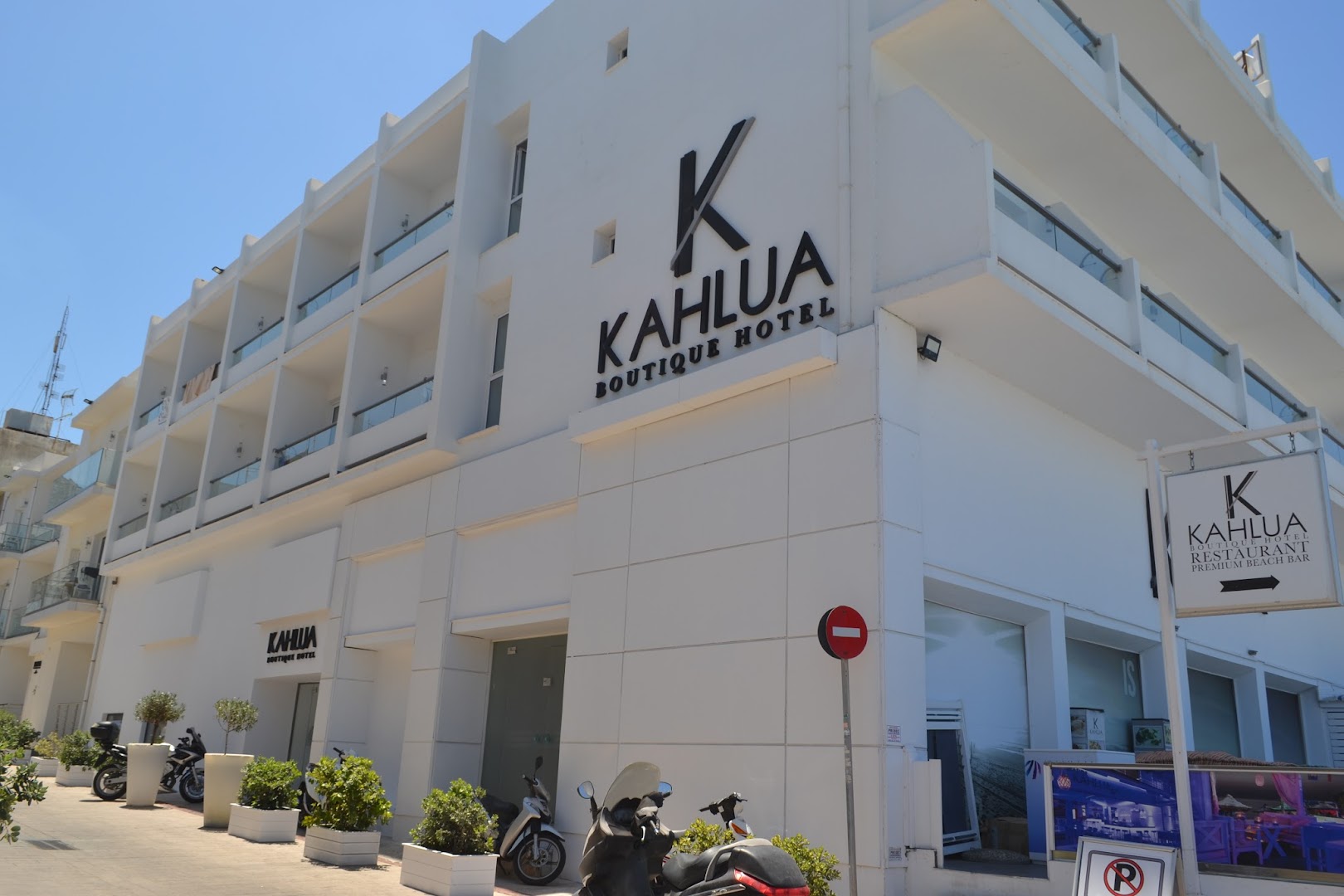 Kahlua Boutique Hotel fasāde dienā — balta daudzstāvu ēka ar balkoniem un restorāna norādi Hersonisas piekrastes ielā