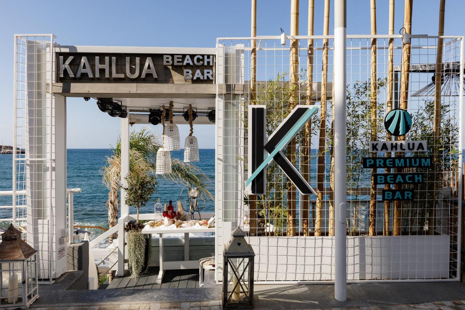 Kahlua Boutique Hotel ieeja Kahlua Premium pludmales bārā Hersonisā, Krētā — skats uz jūru caur stilīgu balta koka konstrukciju