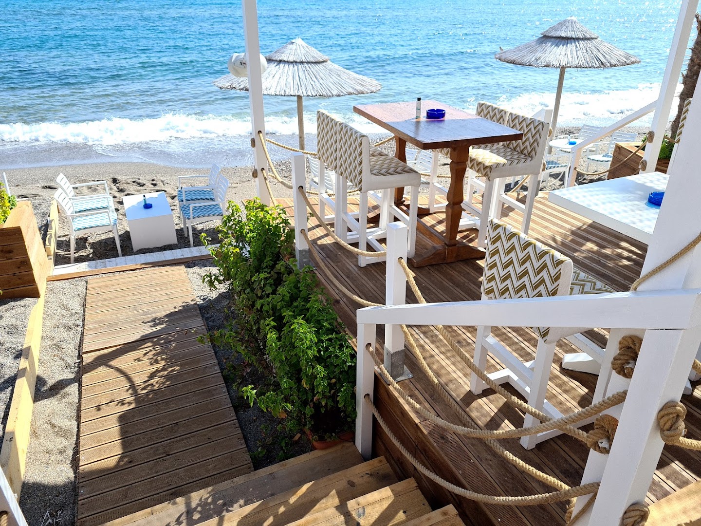 Kahlua Boutique Hotel koka terase ar galdiem un krēsliem pie pludmales — skats uz jūru un saulessargiem Krētā