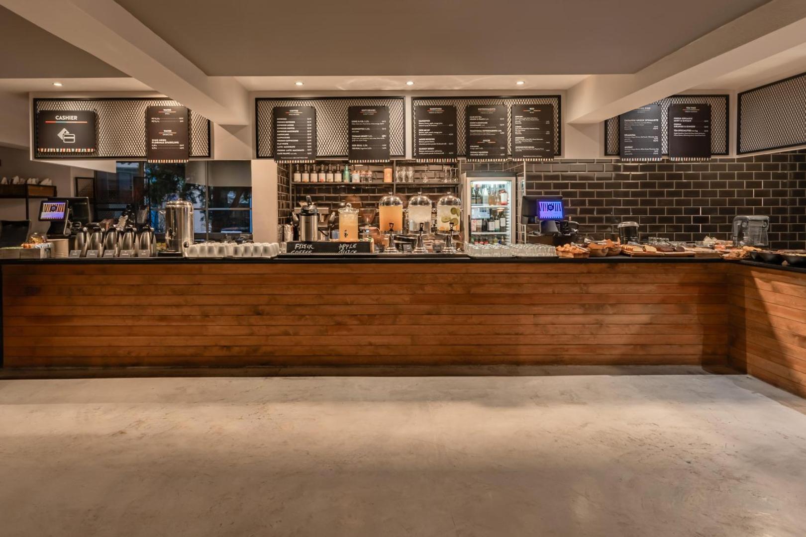 Cook's Club Hersonissos modernā brokastu un dzērienu bufetes zona ar koka apdari, kafijas automātiem un plašu dzērienu izvēli Krētā