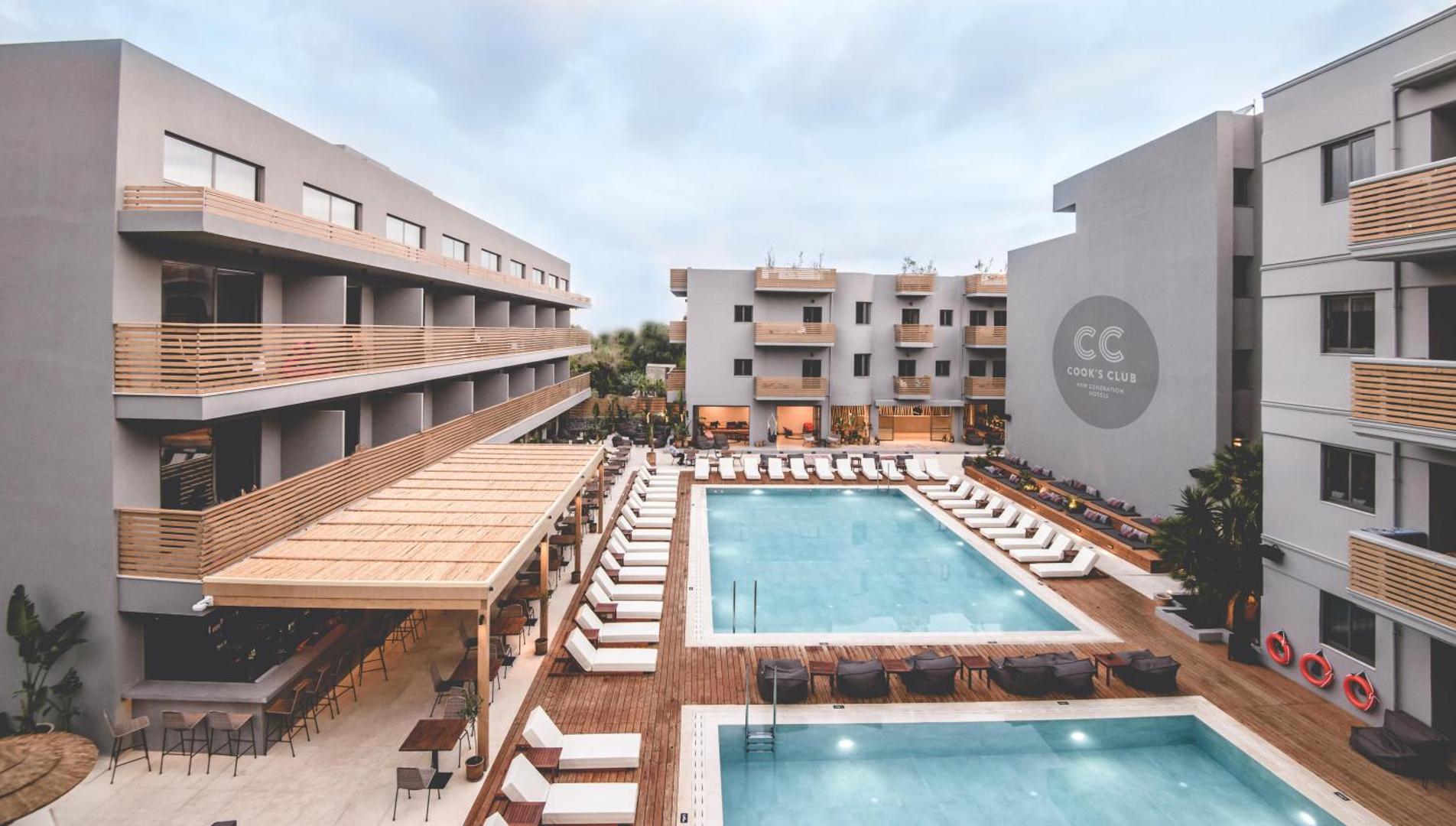 Cook's Club Hersonissos viesnīcas kopskats ar centrālo baseinu, sauļošanās krēsliem un bāru zem nojumes Hersonisā, Krētā