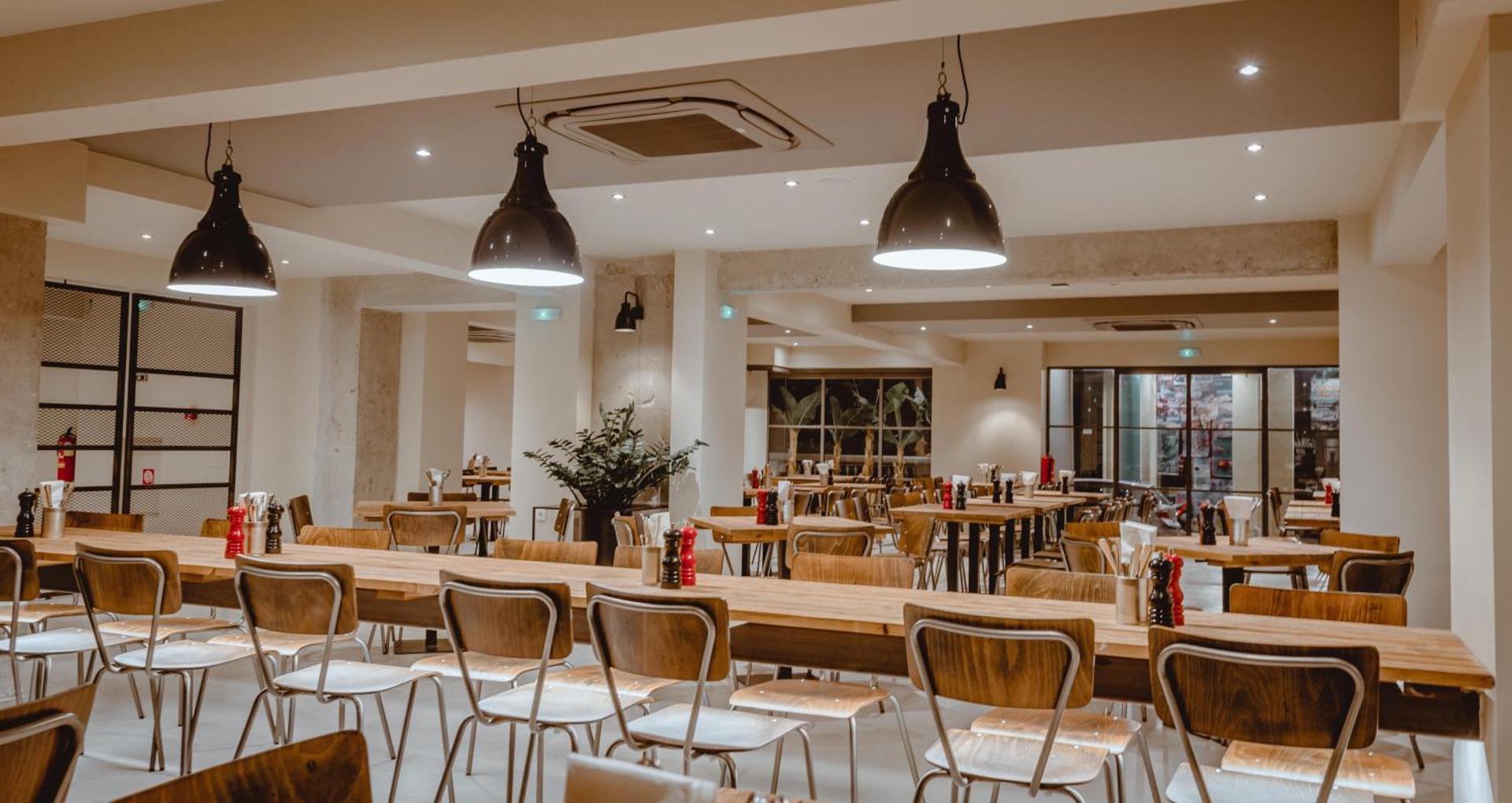 Plašs Cook's Club Hersonissos restorāns ar gariem koka galdiem un modernu apgaismojumu — piemērots lielākām draugu kompānijām