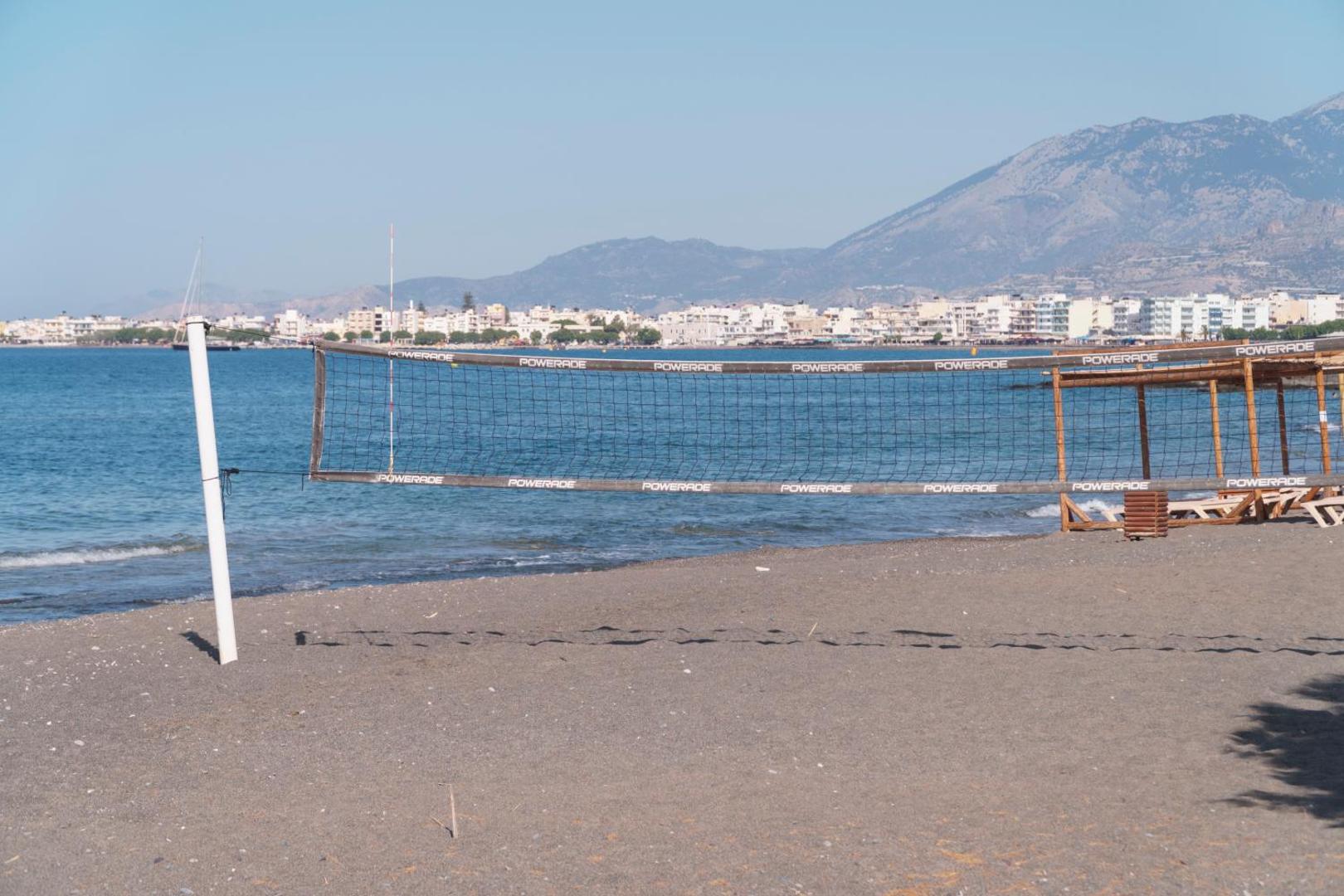 Tylissos Beach Hotel privātā pludmale ar volejbola tīklu smiltīs un skatu uz kalniem un pilsētas piekrasti