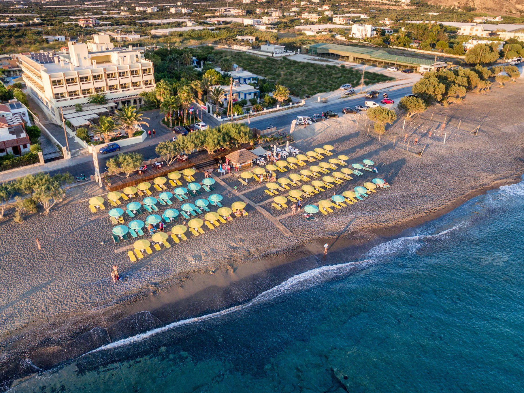 Tylissos Beach Hotel skats no putna lidojuma uz privāto pludmali ar saulessargiem un viesnīcas ēku Ierapetrā, Krētas dienvidos