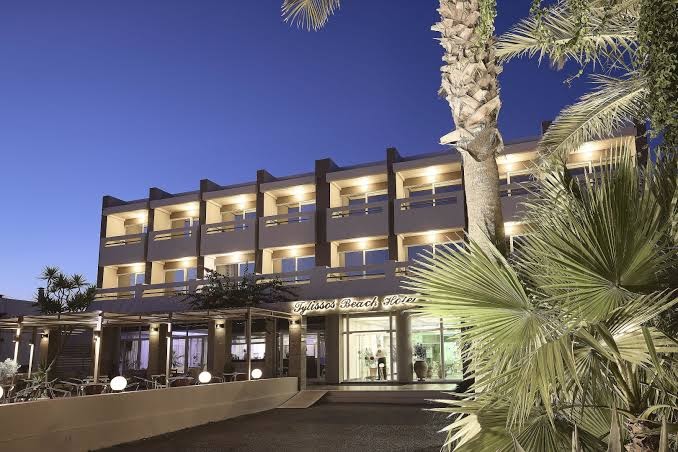 Tylissos Beach Hotel ieeja krēslas stundā ar eksotiskiem augiem un dekoratīvo apgaismojumu — skats uz viesnīcas lobby zonu