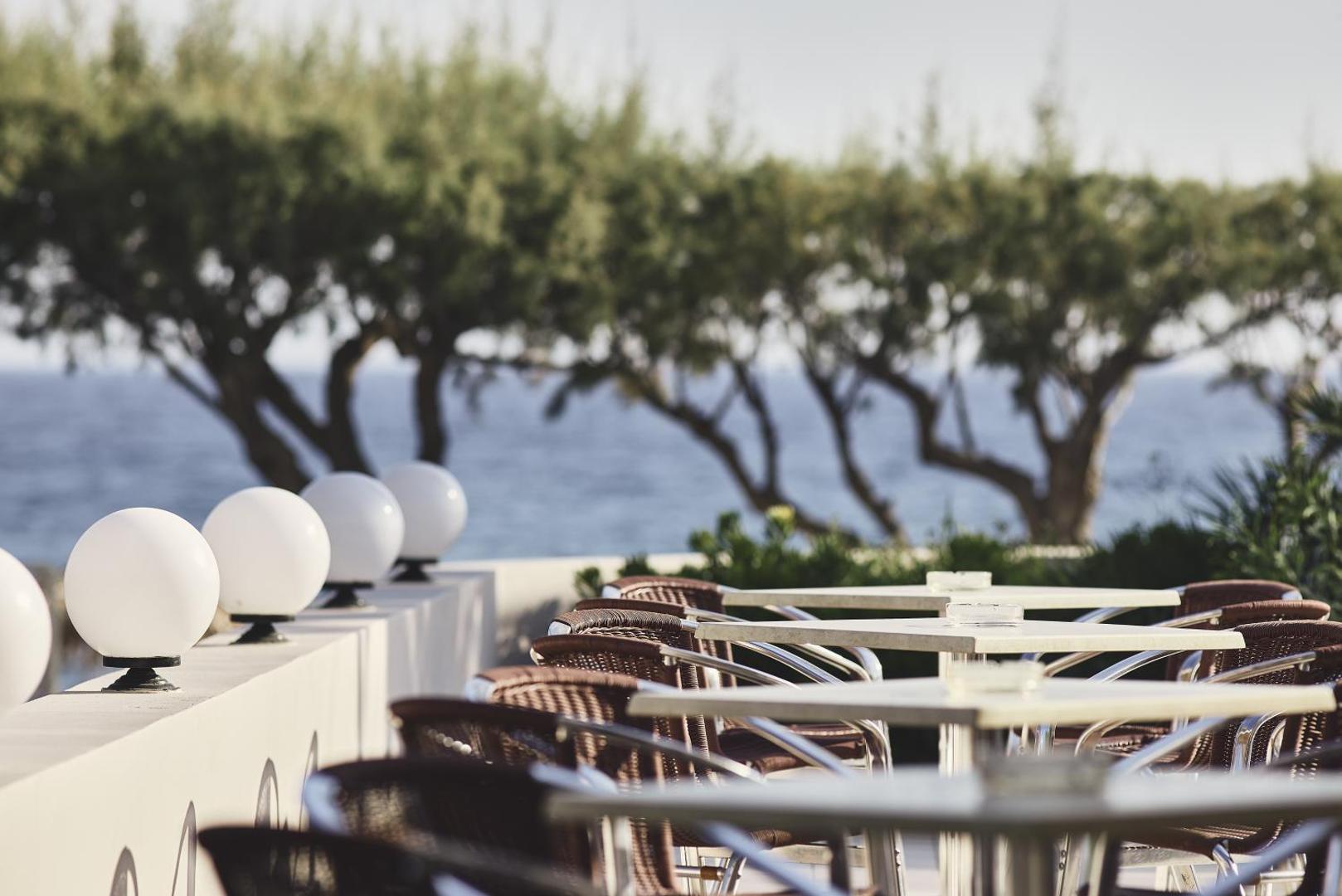 Tylissos Beach Hotel āra terase ar galdiņiem un krēsliem piekrastē, skats uz jūru un kokiem Ierapetrā, Krētā