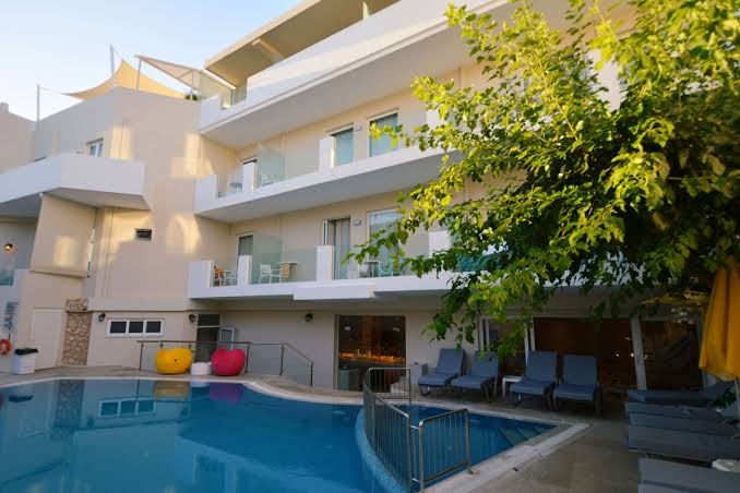 Dimitrios Beach viesnīcas baseins un numuru balkoni dienas gaismā — mājīga iekšpagalma atmosfēra ar zaļojošiem kokiem un atpūtas krēsliem