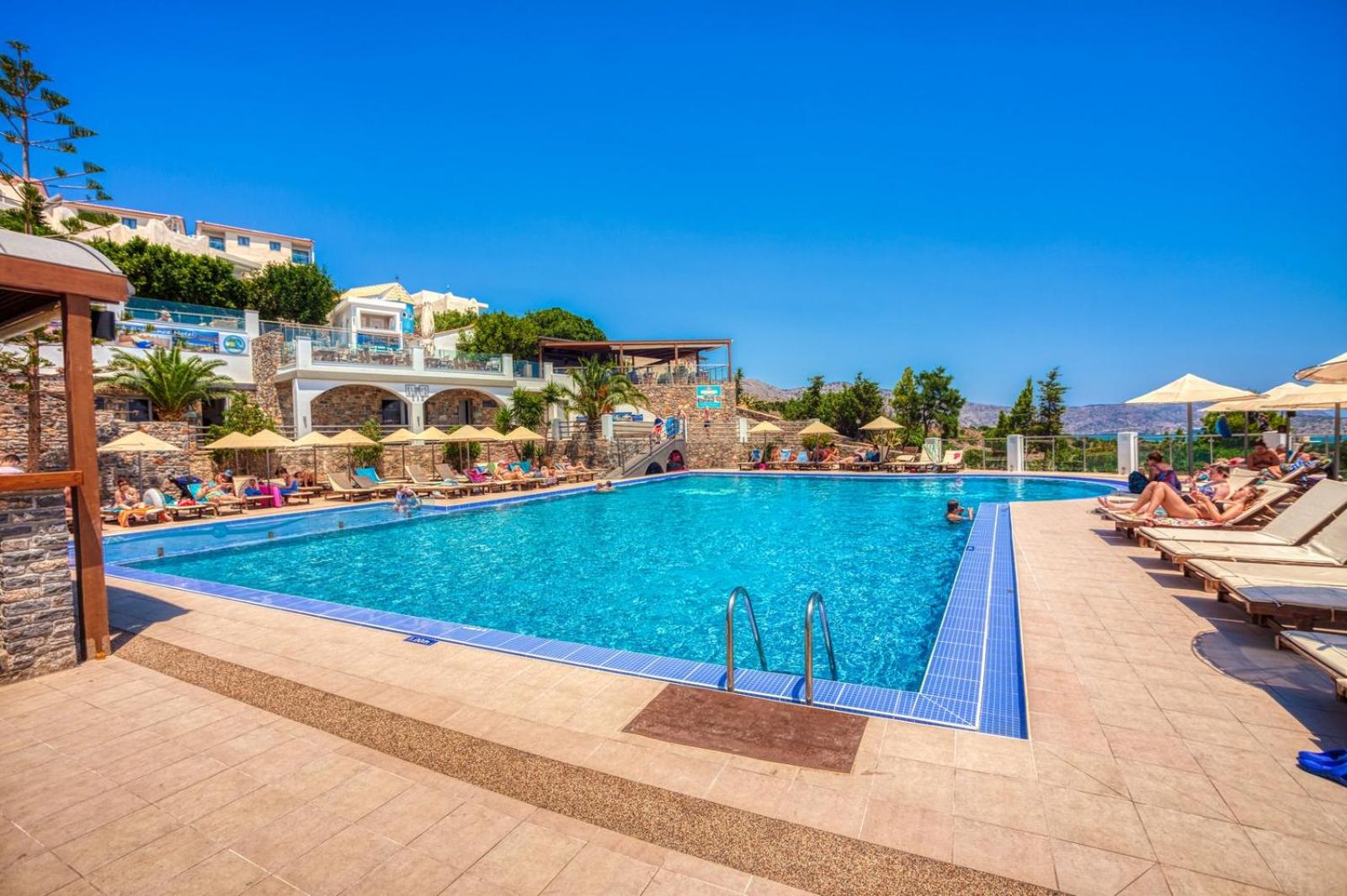 Elounda Waterpark Residence Hotel galvenais āra baseins ar sauļošanās zonu un viesnīcas ēku fonā