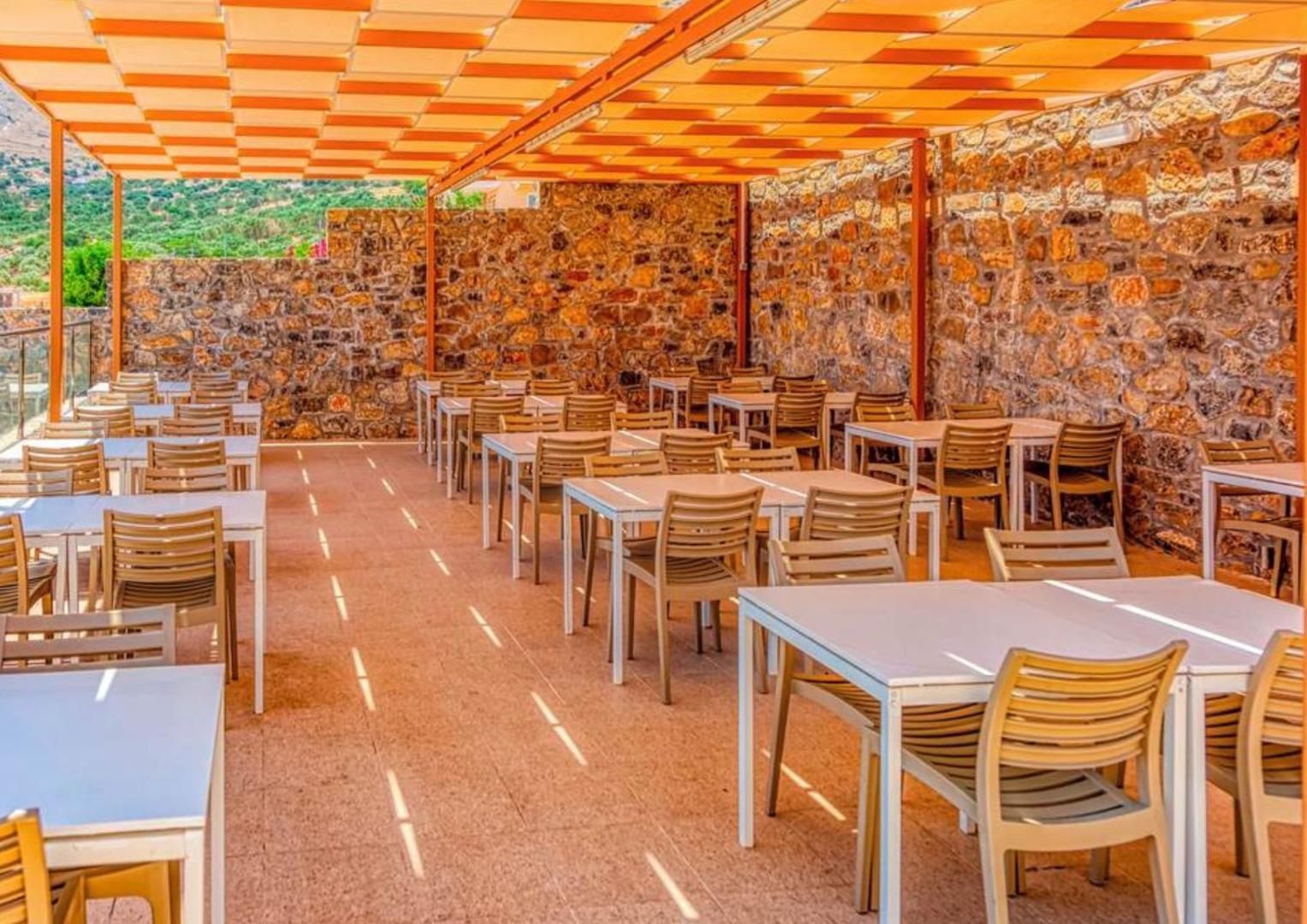 Elounda Waterpark Residence Hotel ēdināšanas zona ar akmens sienām un nojumi, kas nodrošina ēnu karstajās Krētas dienās