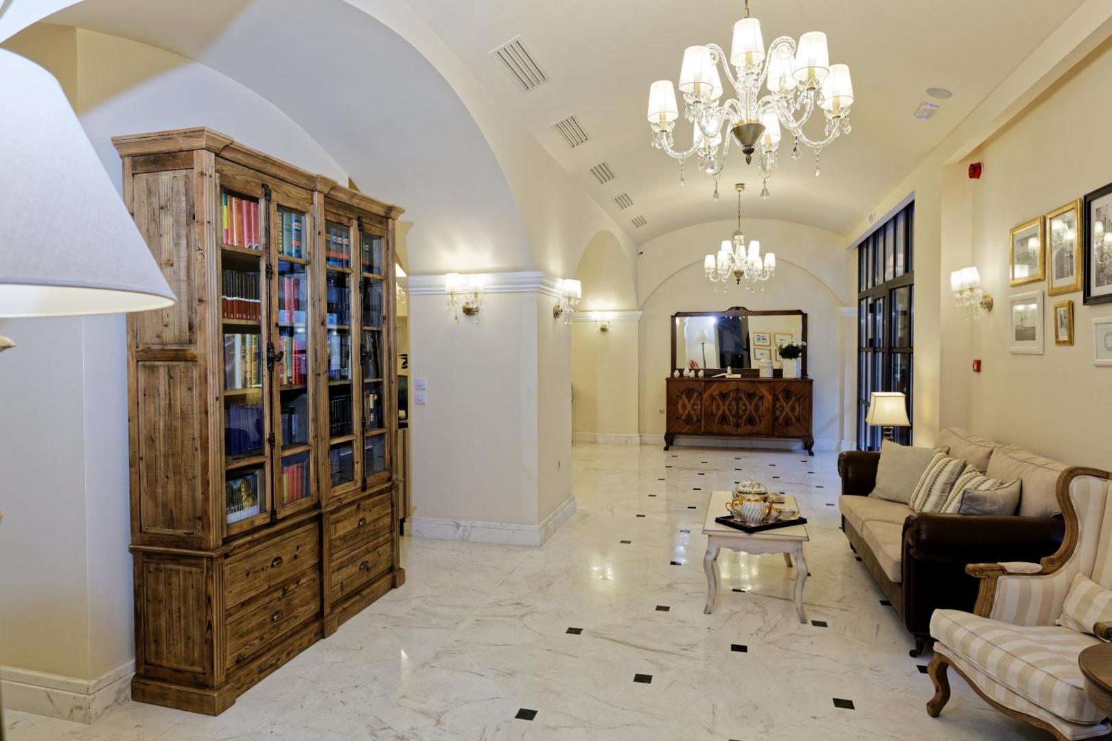 Ionia Suites viesnīcas vestibils Retimno, Krētā ar klasisku koka grāmatplauktu, marmora grīdu un elegantiem atpūtas krēsliem
