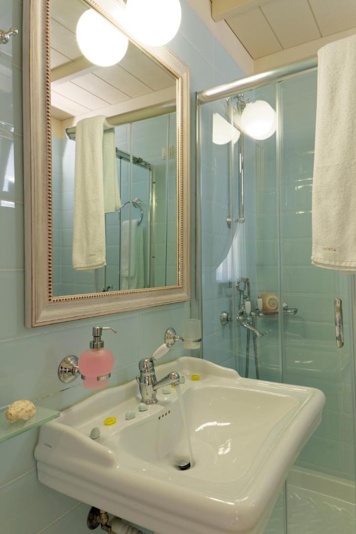 Ionia Suites numura vannas istaba gaiši zilos toņos ar dušas kabīni, lielu spoguli un retro stila santehniku
