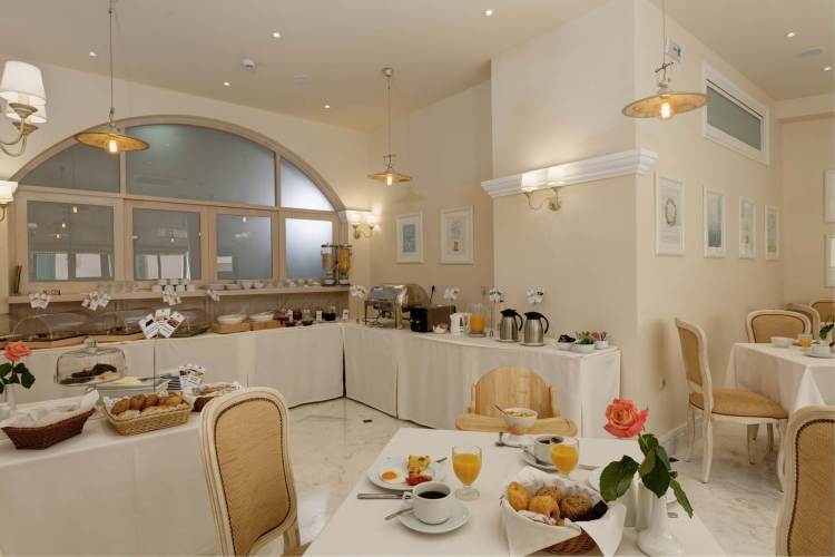 Ionia Suites brokastu zāle ar bagātīgu bufetes galdu, gaišu interjeru, klasiskām mēbelēm un servētiem galdiem viesiem