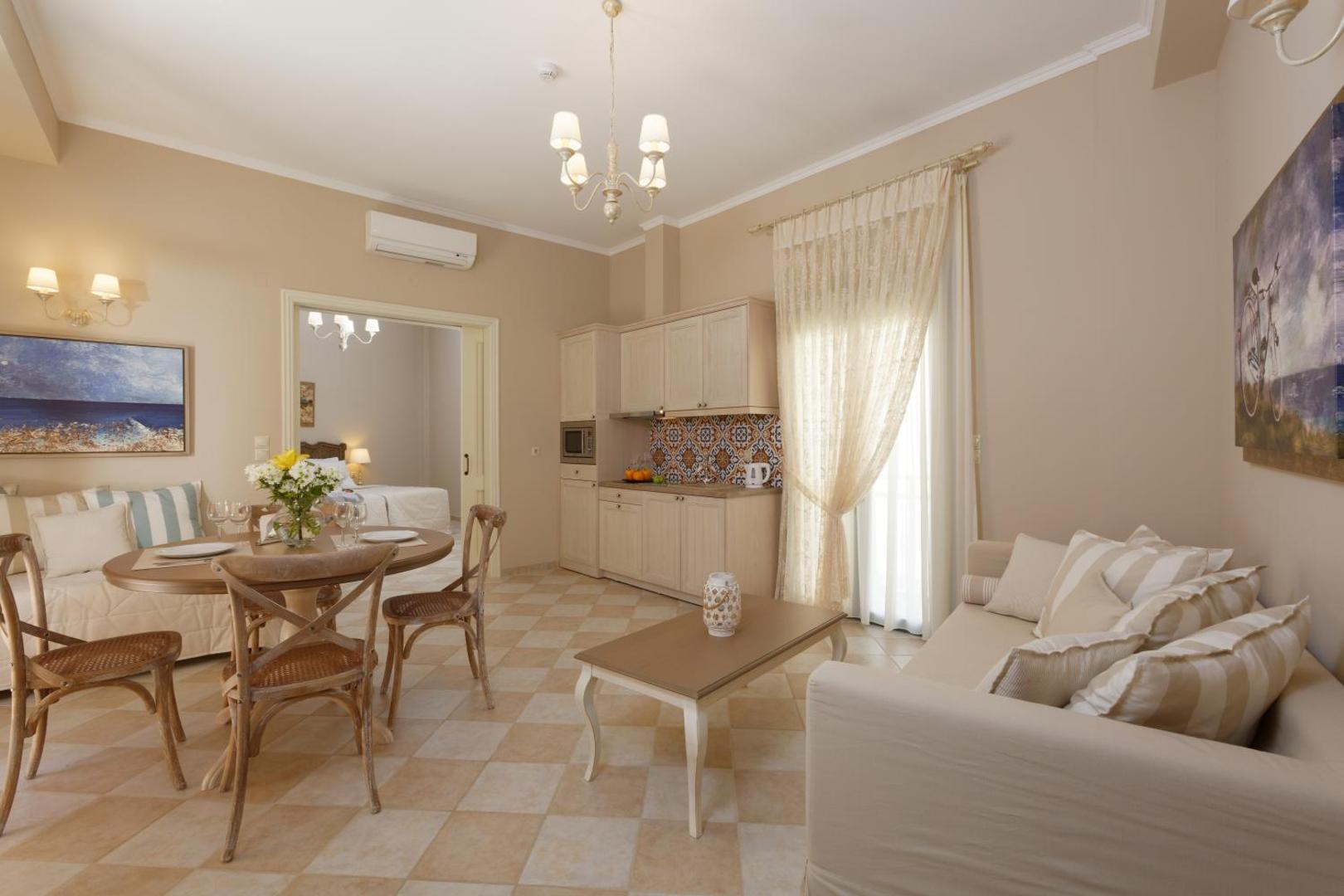 Ionia Suites viesnīcas numurs ar virtuves zonu un viesistabu Retimno, Krētā — gaišs interjers ar dīvānu un pusdienu galdu