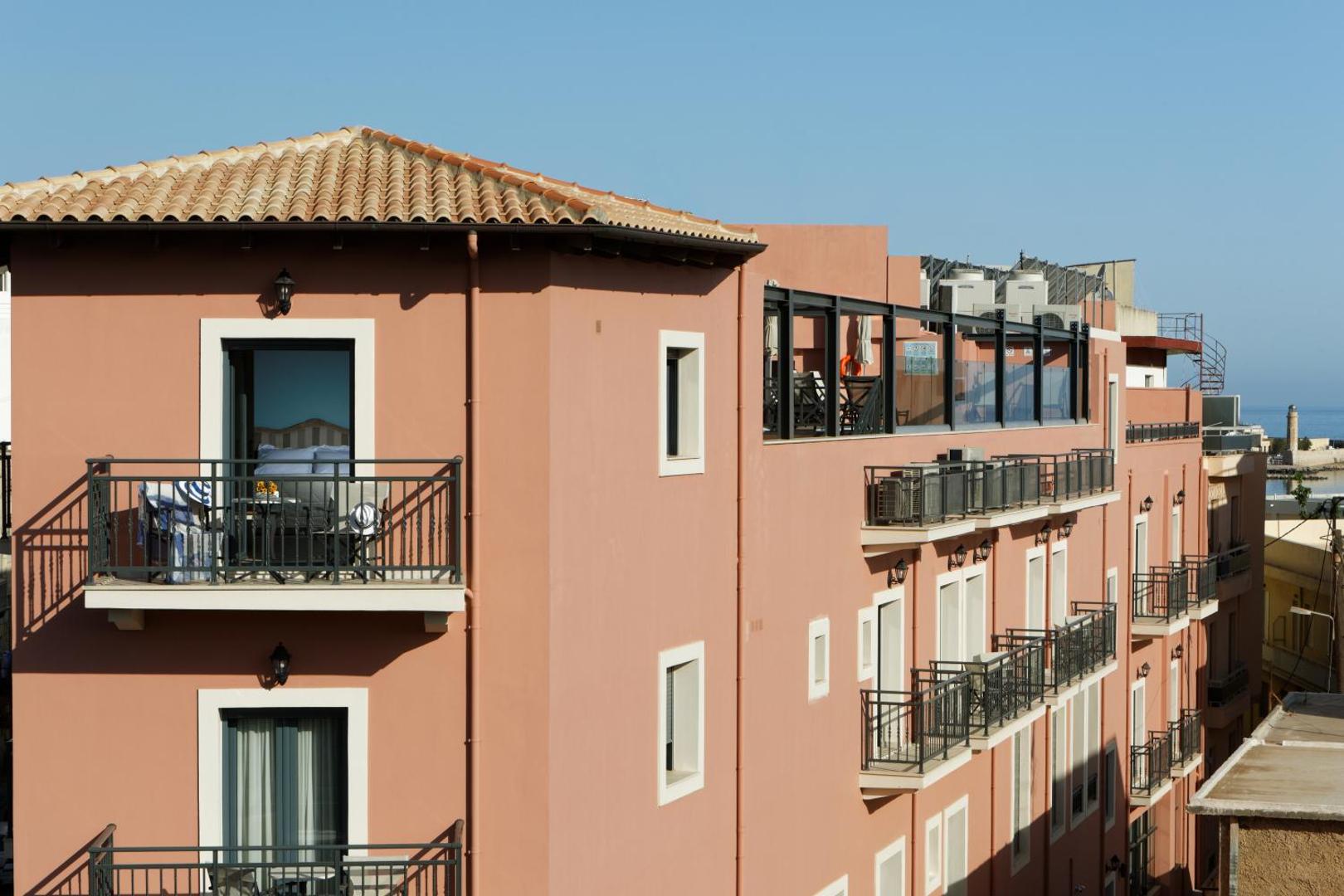 Ionia Suites viesnīcas ēkas skats no augšas ar balkoniem un jumta terasi Retimno, fonā redzama jūra un pilsētas osta