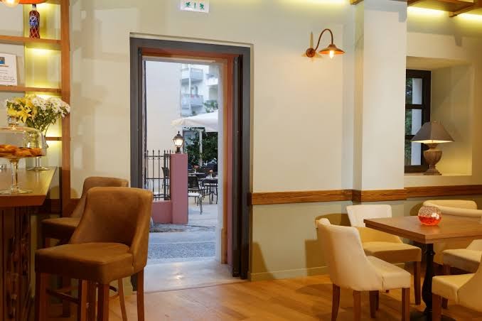 Ionia Suites bāra zona ar skatu uz āra terasi, koka galdiem un mīkstiem krēsliem