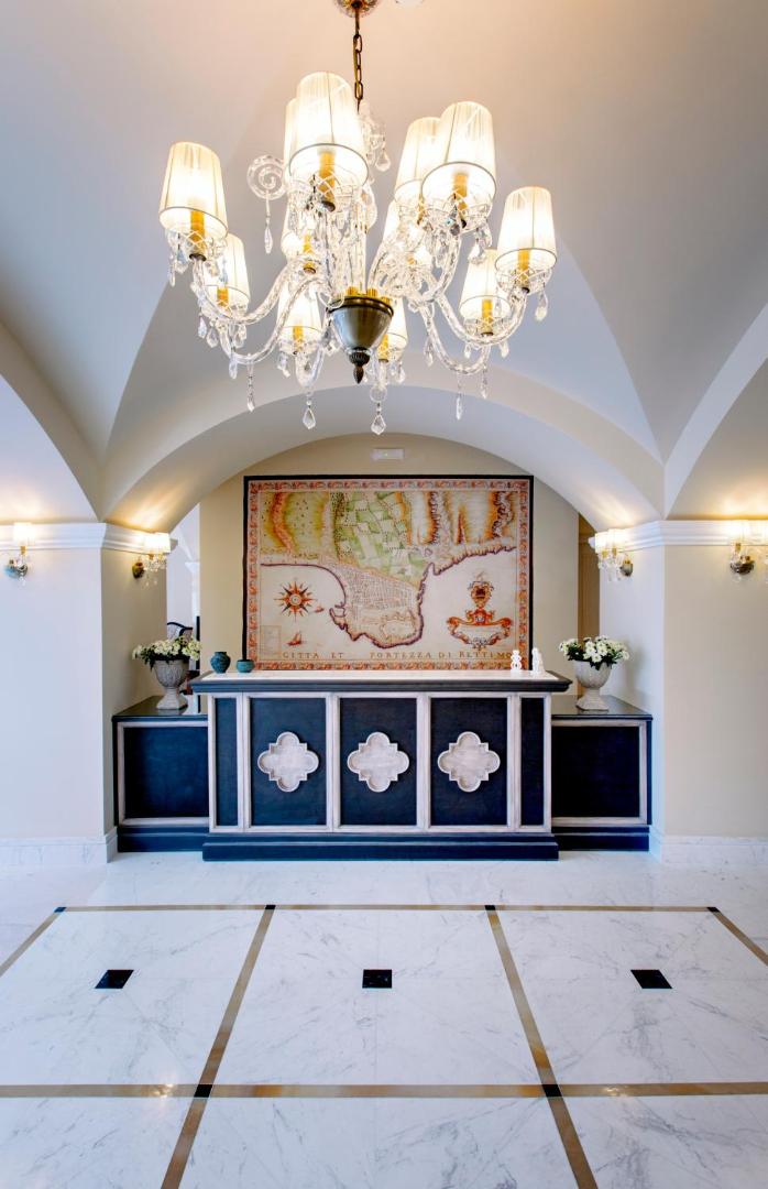Ionia Suites viesnīcas eleganta recepcijas zona ar klasisku leti, lielu vēsturisku karti pie sienas un greznu lustru