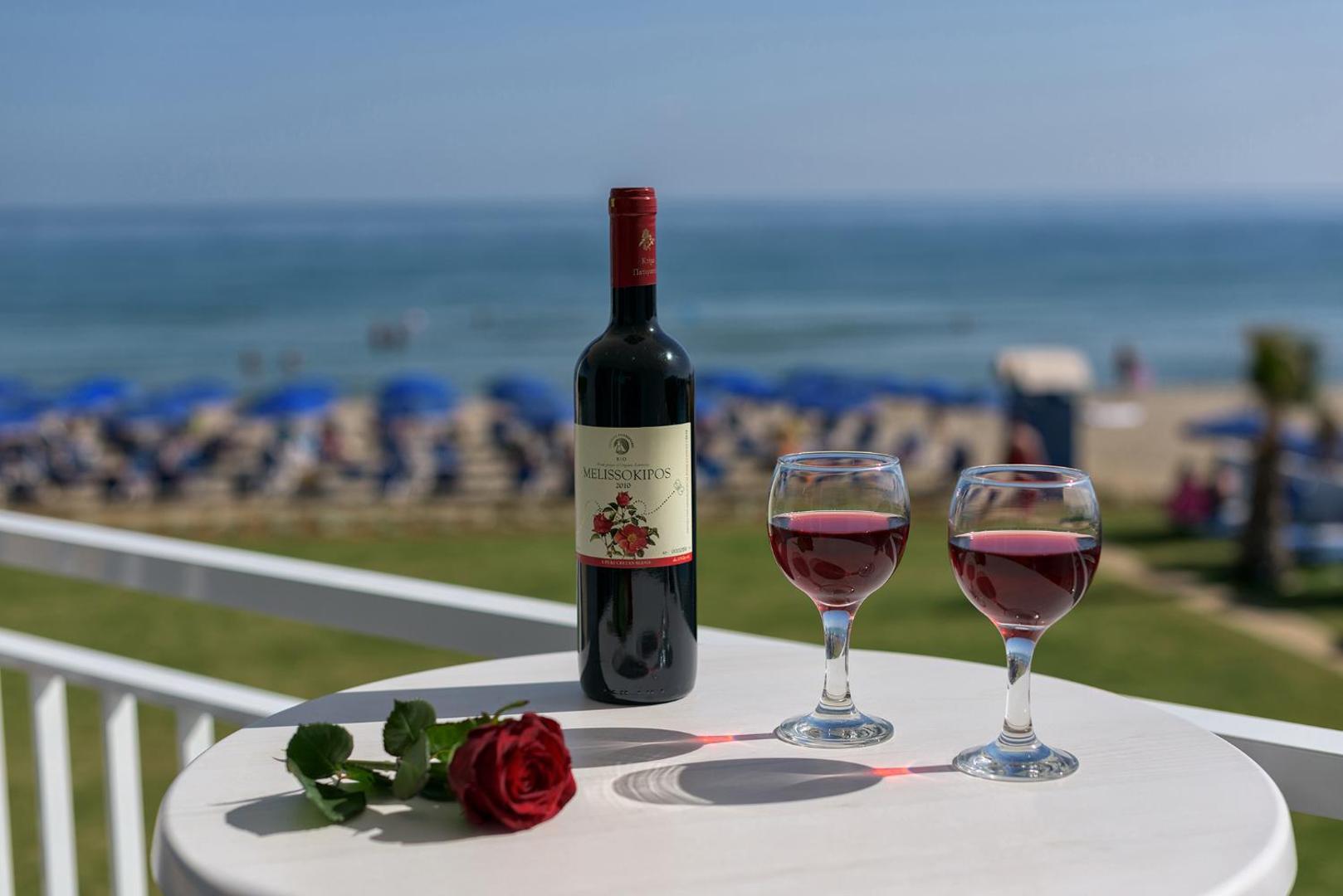 Vīna pudele un divas glāzes uz galda ar skatu uz Happy Days Beach privāto pludmali un zilo jūru Krētā
