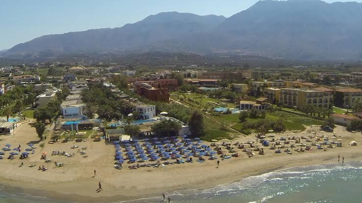 Happy Days Beach viesnīcas panorāmas skats no putna lidojuma uz pludmali, ziliem saulessargiem un kalniem fonā