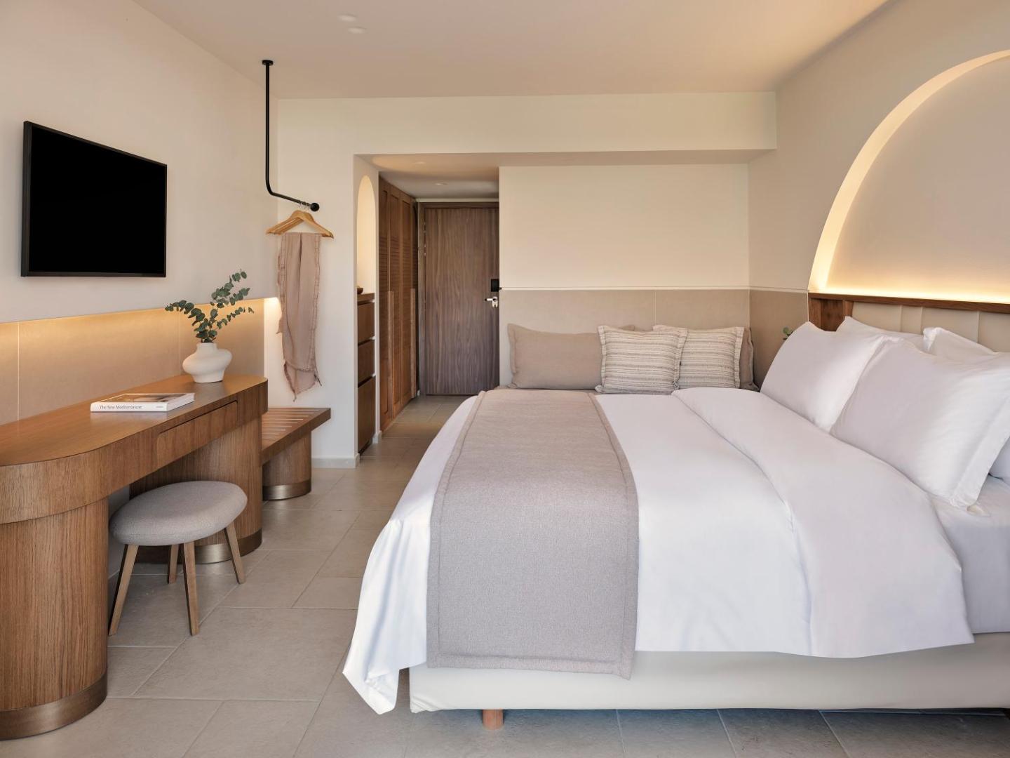 Lindos Princess Beach Hotel moderns numurs ar gaišu interjeru, koka mēbelēm, sienas televizoru un ērtu divguļamo gultu Rodas salā.