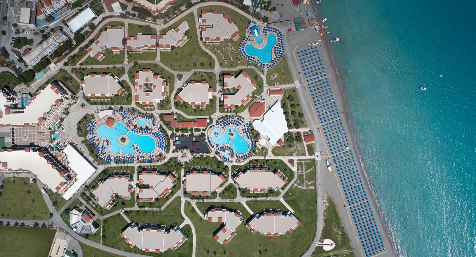 Lindos Princess Beach Hotel aerofoto skats uz viesnīcas plānojumu, baseiniem un garo piekrastes joslu ar saulessargiem Rodā.