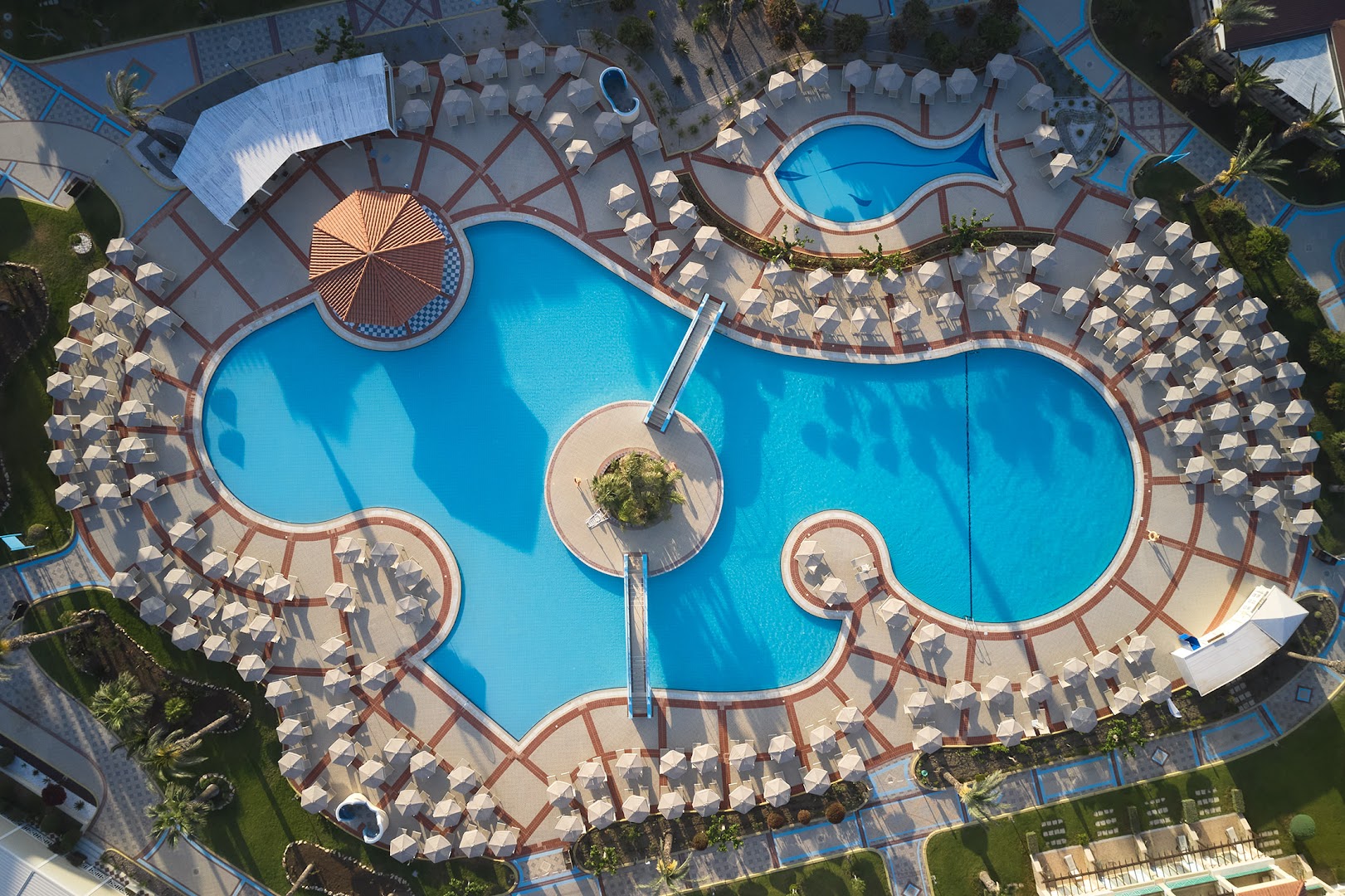 Lindos Princess Beach Hotel aerofoto ar centrālo baseinu kompleksu — simtiem gaišu saulessargu, tiltiņi un bērnu ūdens slidkalniņi