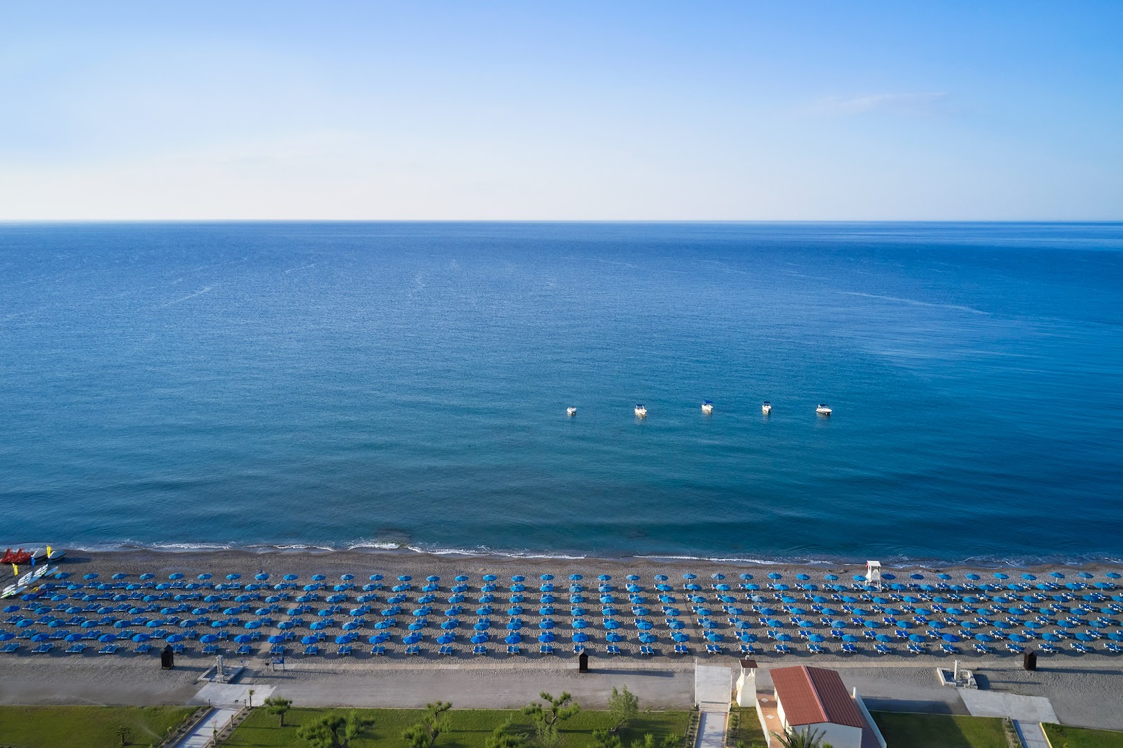 Lindos Princess Beach Hotel privātā pludmale no putna lidojuma Rodā — zili saulessargi, dzidrs jūras ūdens un plaša krasta līnija
