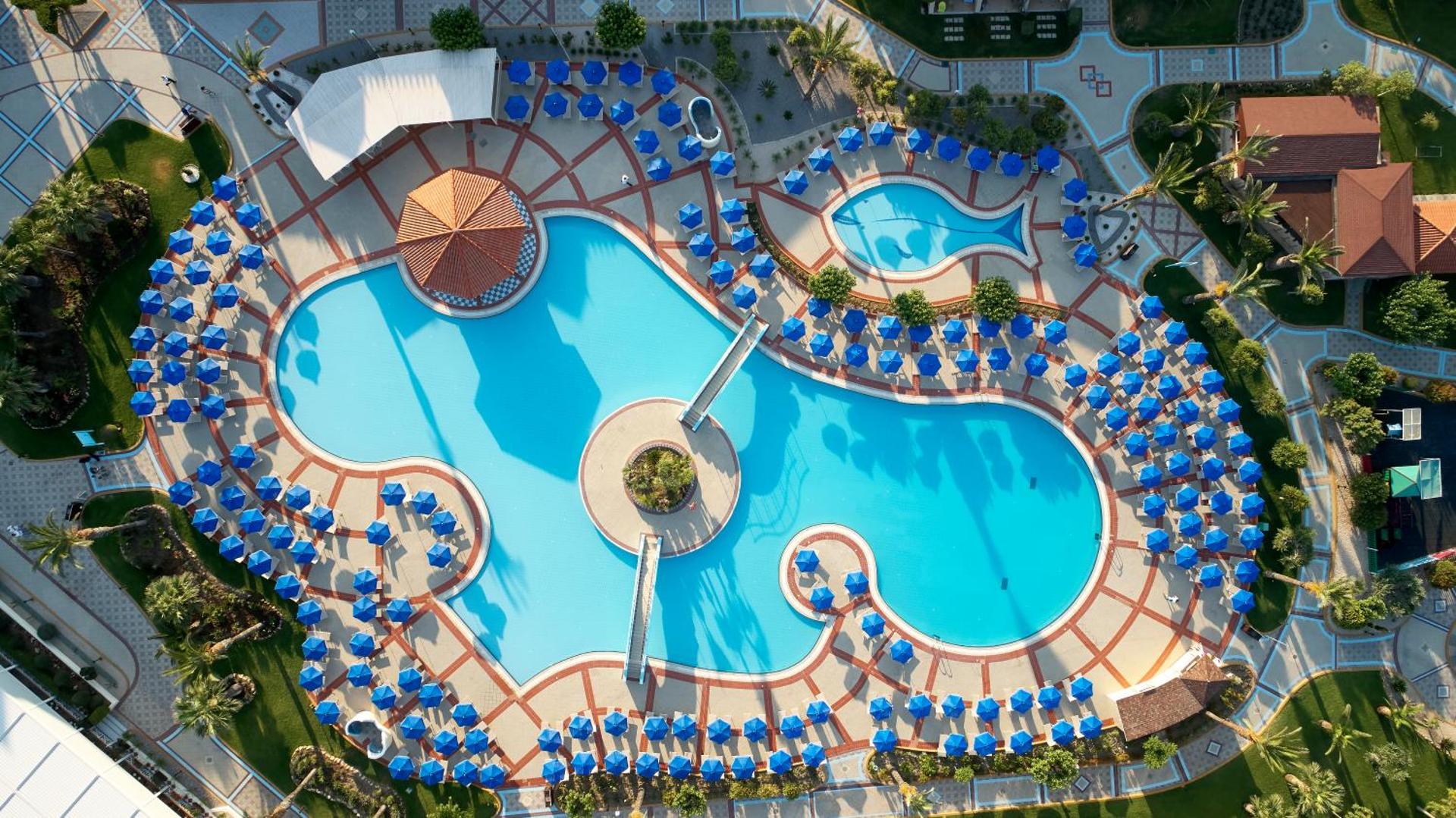 Lindos Princess Beach Hotel plašā baseinu teritorija no putna lidojuma Rodā — vairāki baseini, tiltiņi, bārs un simtiem sauļošanās vietu