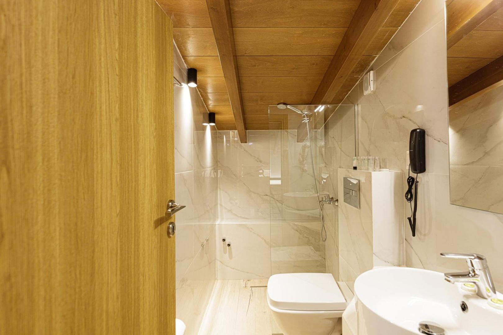 Filion Suites Resort & Spa gaiša vannas istaba ar koka griestu sijām, marmora flīzēm un stikla dušas kabīni Krētā