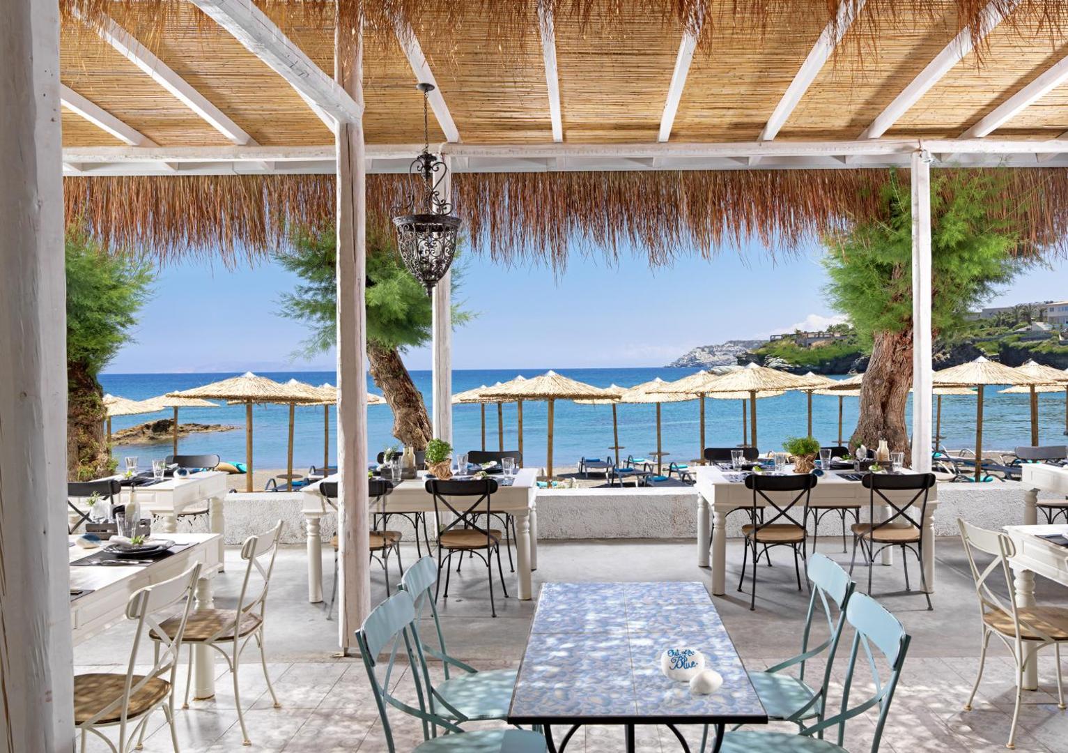 Out Of The Blue Resort & Spa brīvdabas restorāns ar skatu uz jūru, baltiem galdiem un tradicionālu niedru jumta segumu