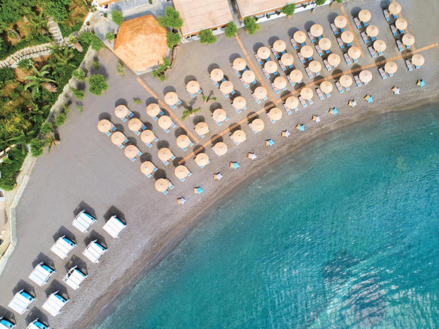 Out Of The Blue Resort & Spa privātā pludmale no putna lidojuma — saulessargi un sauļošanās krēsli pie dzidra ūdens