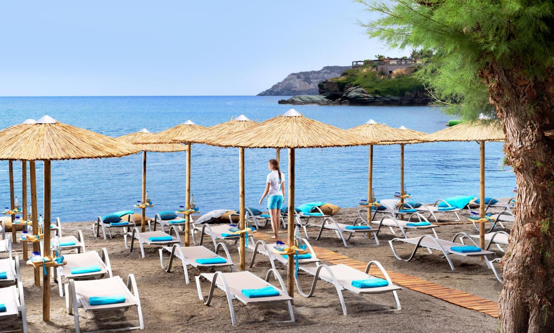 Viesnīcas Out Of The Blue Resort & Spa pludmales zona ar sakārtotiem zviļņiem, gaiši ziliem dvieļiem un salmu saulessargiem
