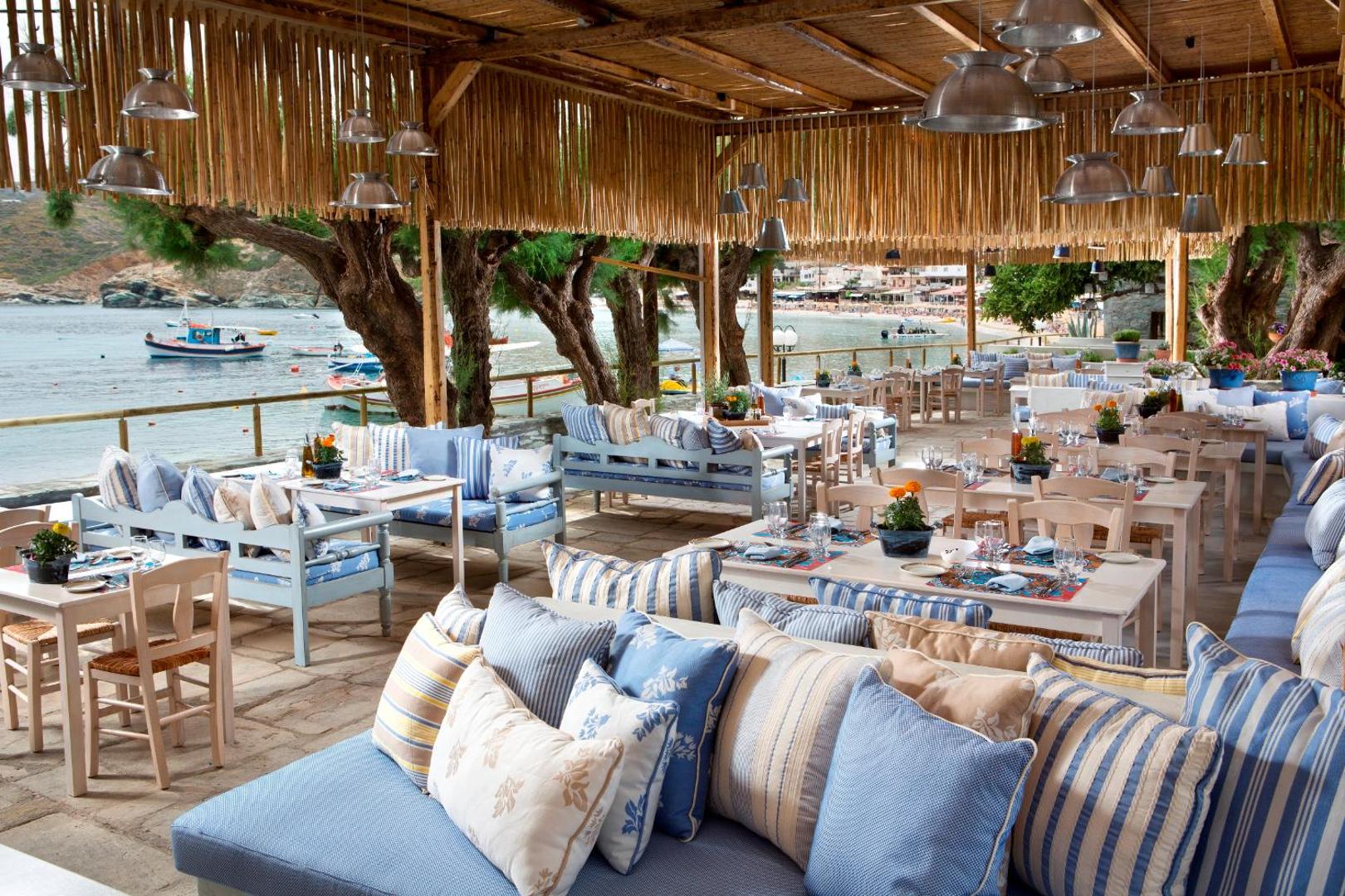 Mājīga Out Of The Blue Resort & Spa terase ar mīkstiem dīvāniem, svītrainiem spilveniem un skatu uz zvejas laivām līcī