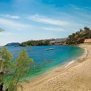 Panorāmas skats uz Out Of The Blue Resort & Spa smilšu pludmali un kūrorta ēkām piekrastes kalna galā Krētā