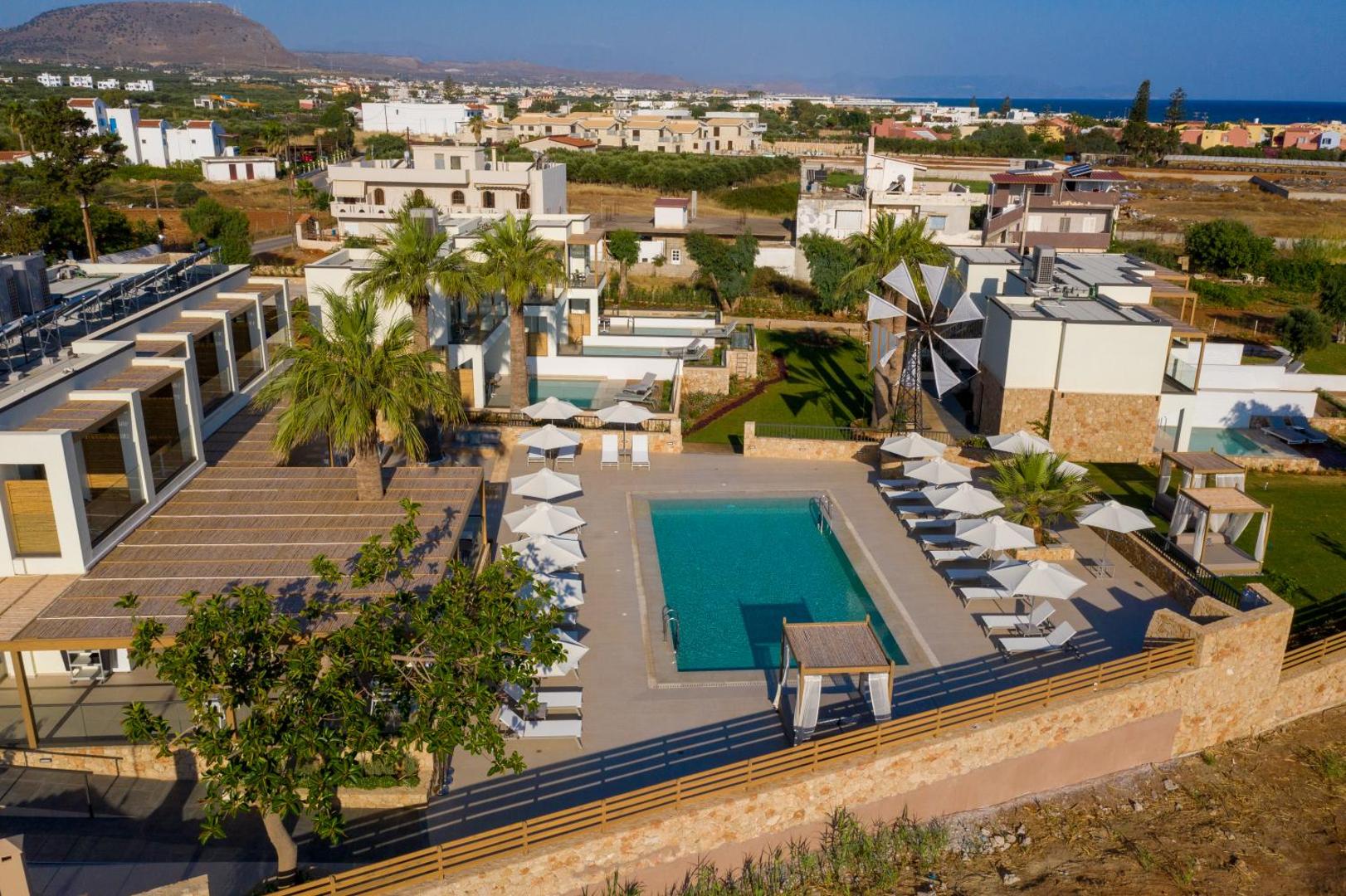 Aloe Boutique Hotel āra baseins ar sauļošanās krēsliem un saulessargiem — apkārtnē palmas, dekoratīvas vējdzirnavas un zāliens
