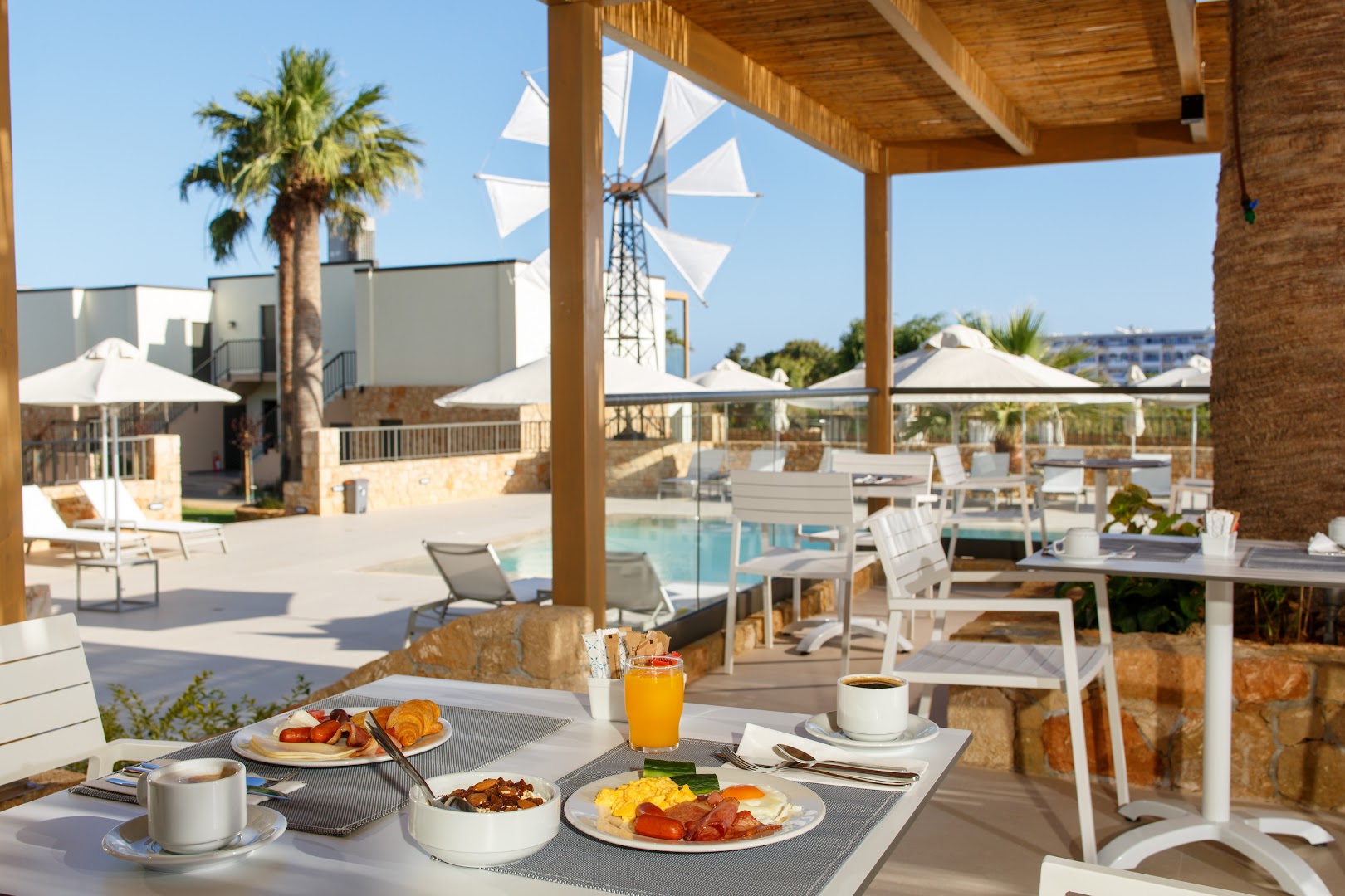 Aloe Boutique Hotel āra terase ar skatu uz baseinu un vējdzirnavām, kur tiek pasniegtas brokastis Stalidā, Krētā