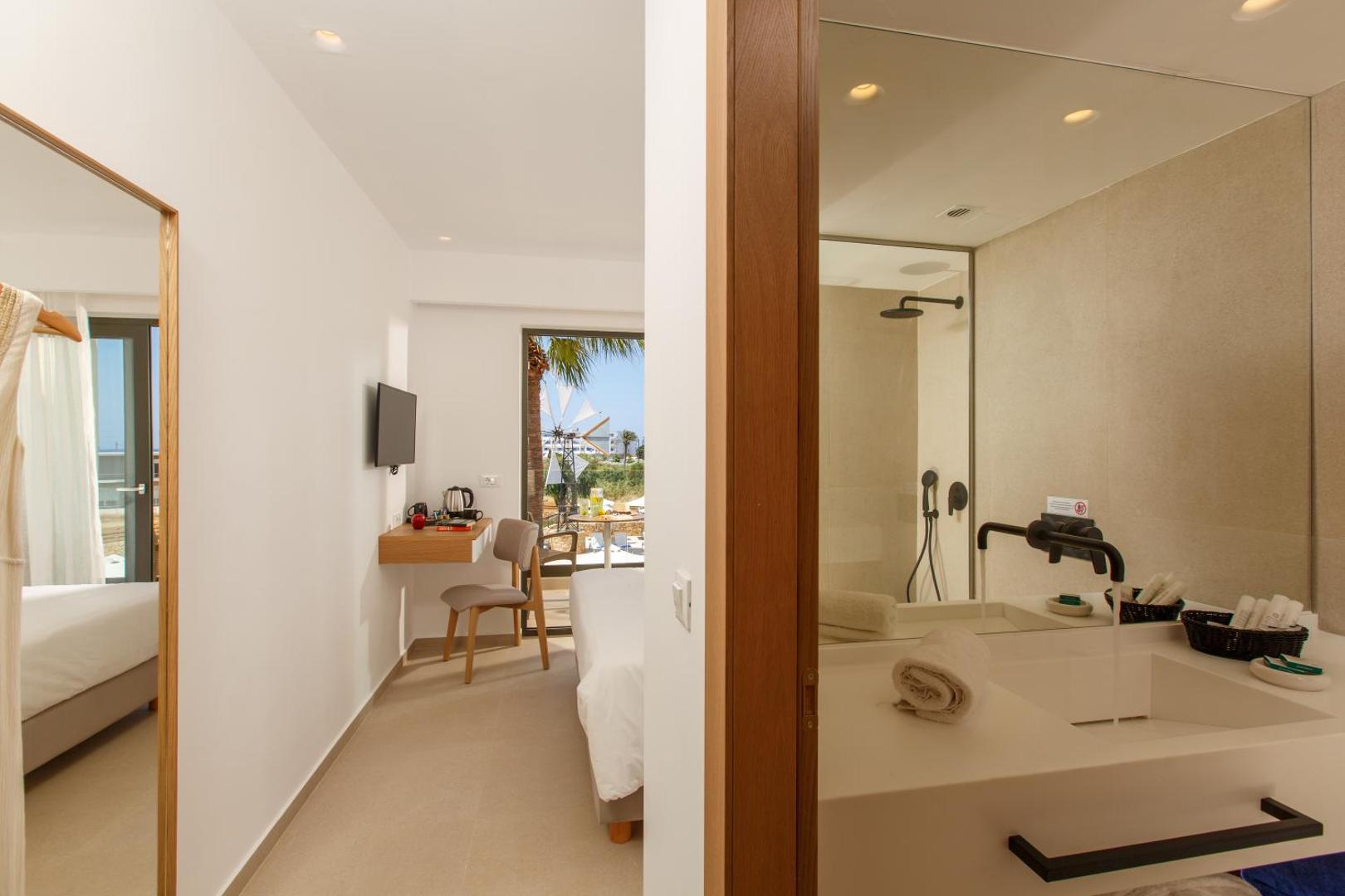 Aloe Boutique Hotel numura interjers ar skatu uz vannas istabu un darba zonu, fonā redzamas vējdzirnavas