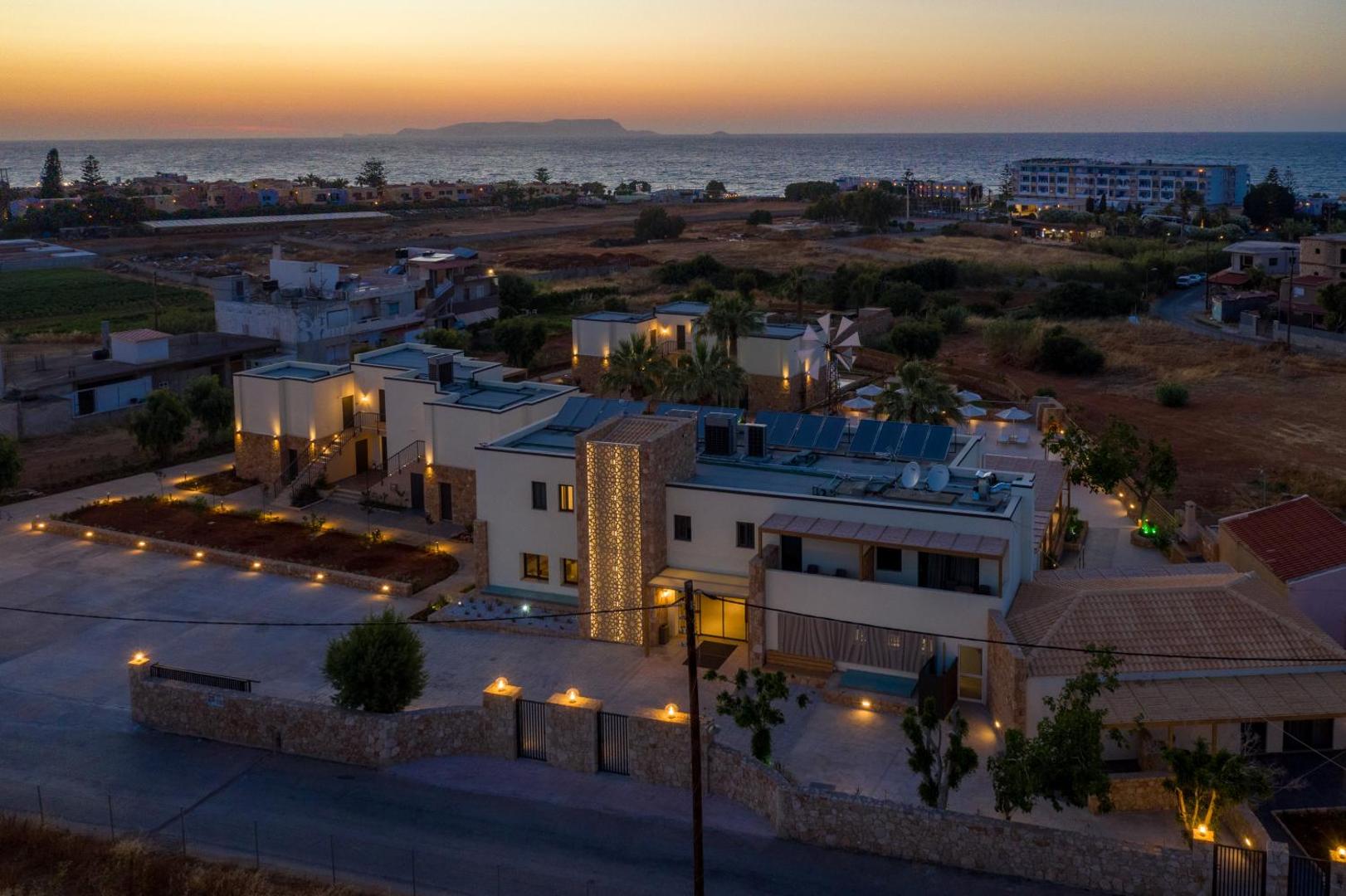 Aloe Boutique Hotel Powered By Anissa skats no putna lidojuma saulrietā — izgaismota viesnīcas ēka piekrastē ar skatu uz jūru