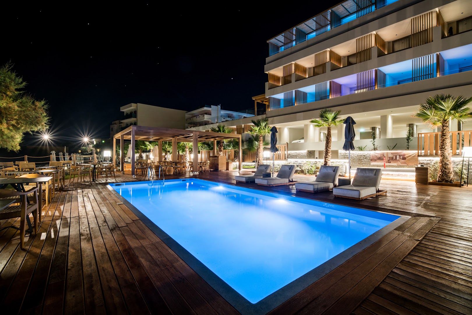 Akasha Beach Hotel & Spa izgaismots āra baseins naktī ar koka terasi, sauļošanās krēsliem un restorāna zonu fonā