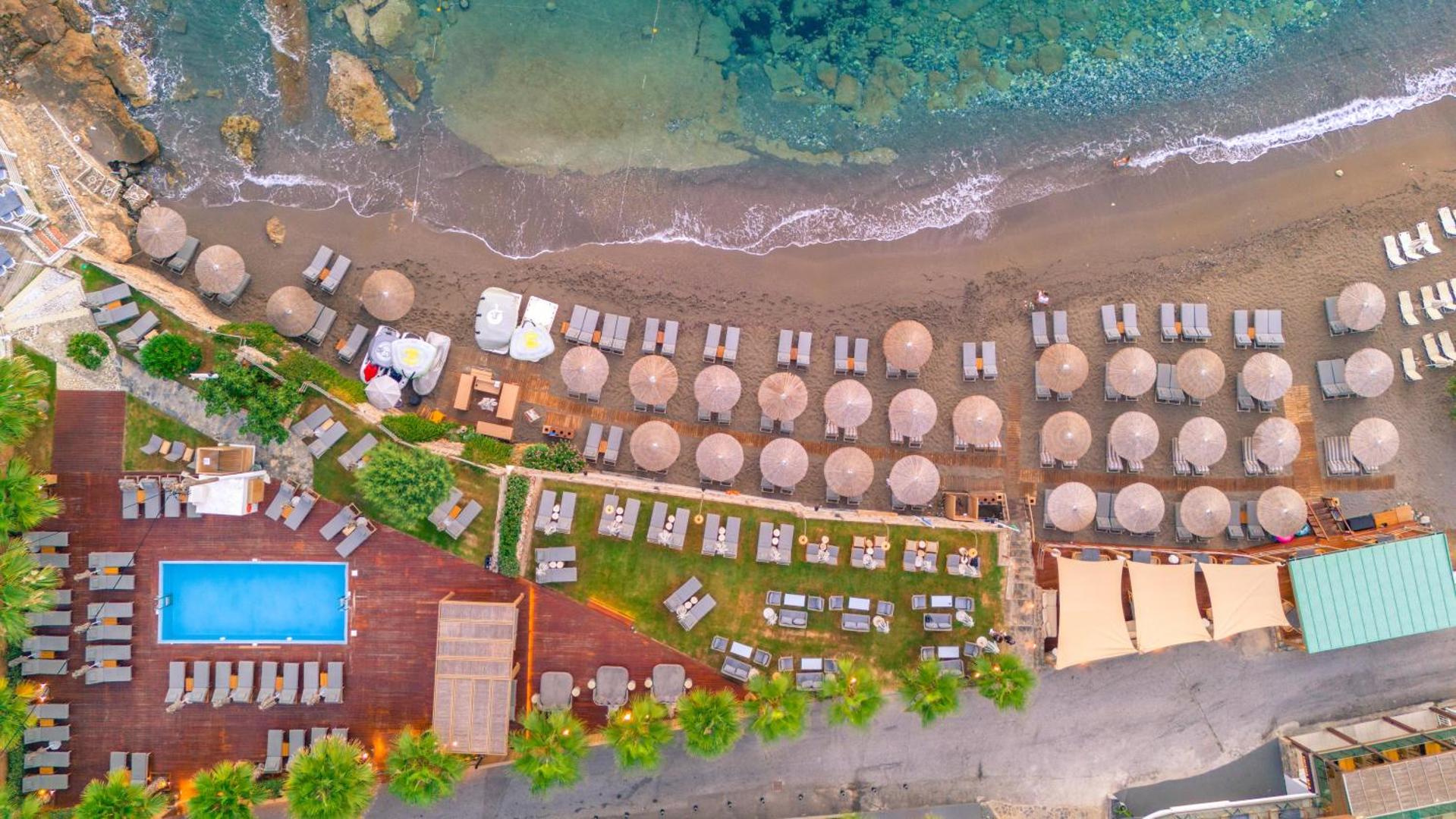 Akasha Beach Hotel & Spa skats no putna lidojuma uz privāto pludmali Hersonisā, Krētā — saulessargi, zviļņi un āra baseins pie krasta