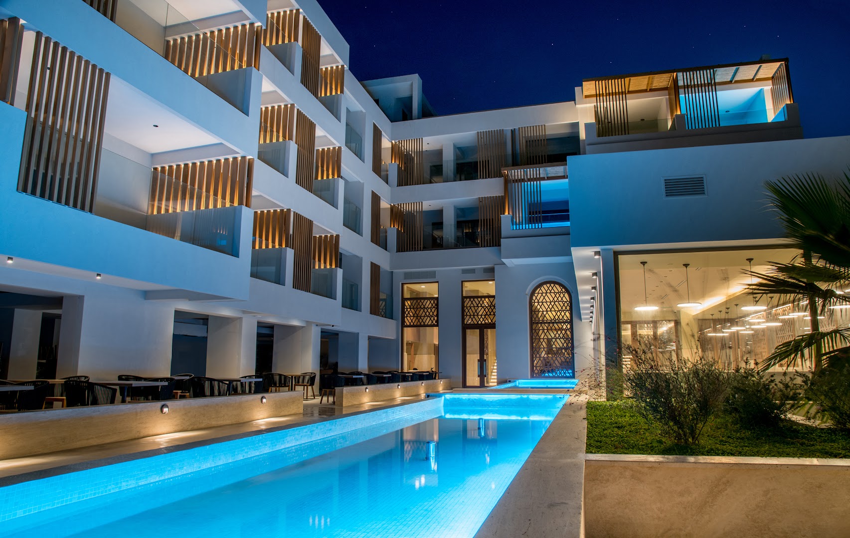 Akasha Beach Hotel & Spa fasāde un izgaismots dekoratīvais baseins vakarā — moderni numuri ar balkoniem un siltu apgaismojumu