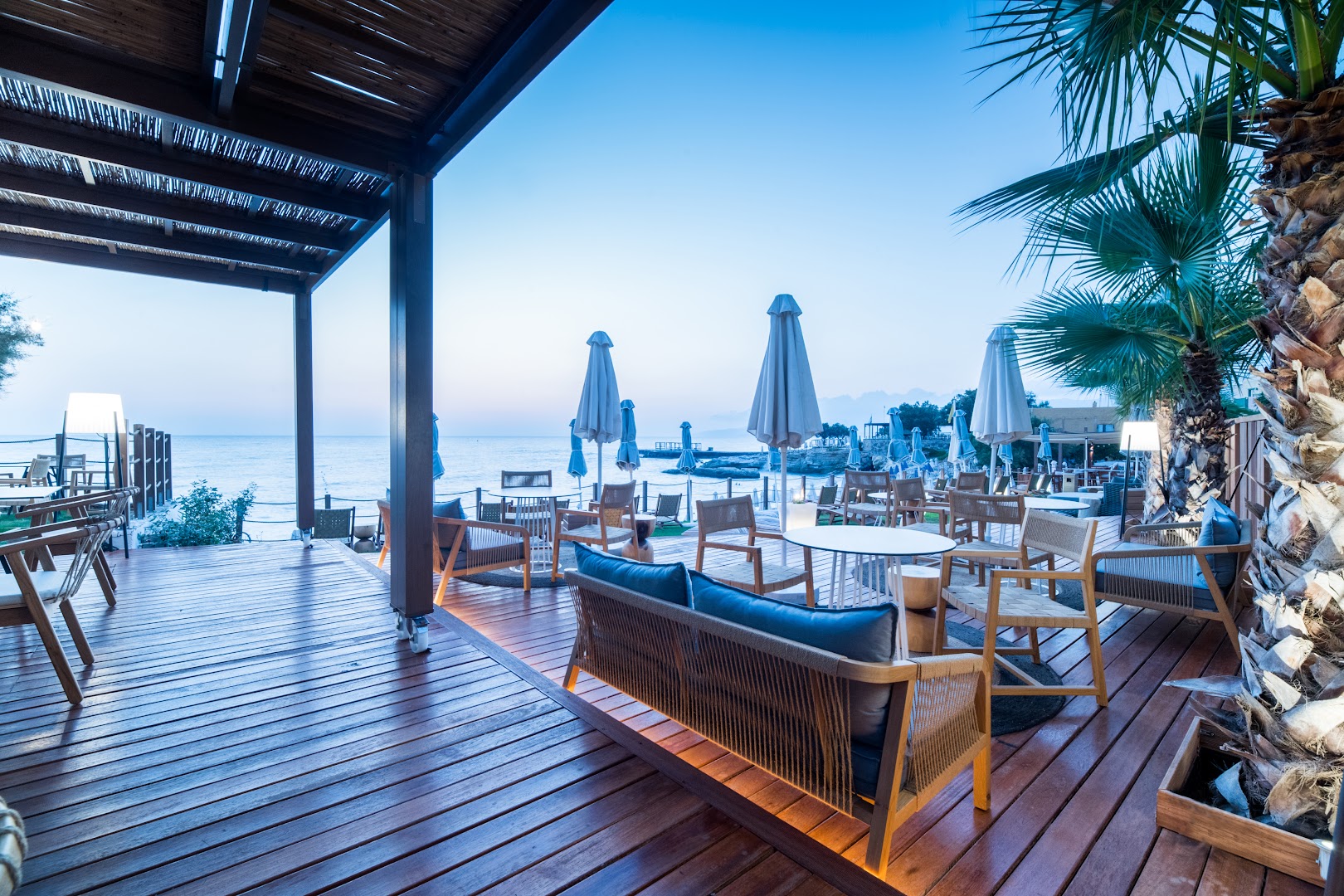 Akasha Beach Hotel & Spa āra terase ar koka klāju un stilīgām mēbelēm Hersonisā, Krētā — skats uz jūru saulrietā