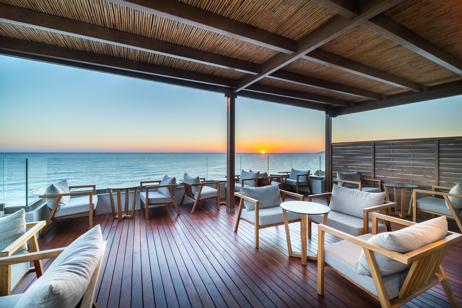 Akasha Beach Hotel & Spa āra terase ar skatu uz Vidusjūru saulrieta laikā — koka klājs un ērtas mēbeles