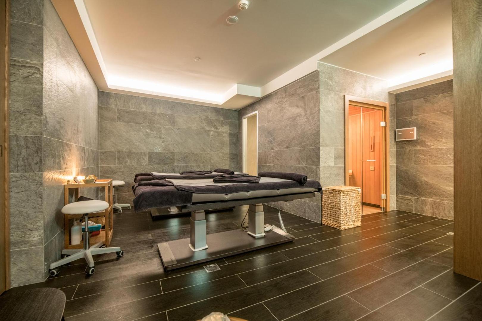 Akasha Beach Hotel & Spa modernā spa procedūru telpa ar masāžas galdiem un akmens apdari mierpilnai atpūtai Krētā