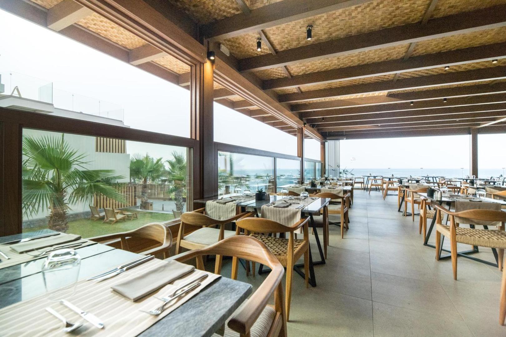 Akasha Beach Hotel & Spa gaišs ēdienkartes restorāns ar panorāmas logiem un skatu uz palmu dārzu un Vidusjūru