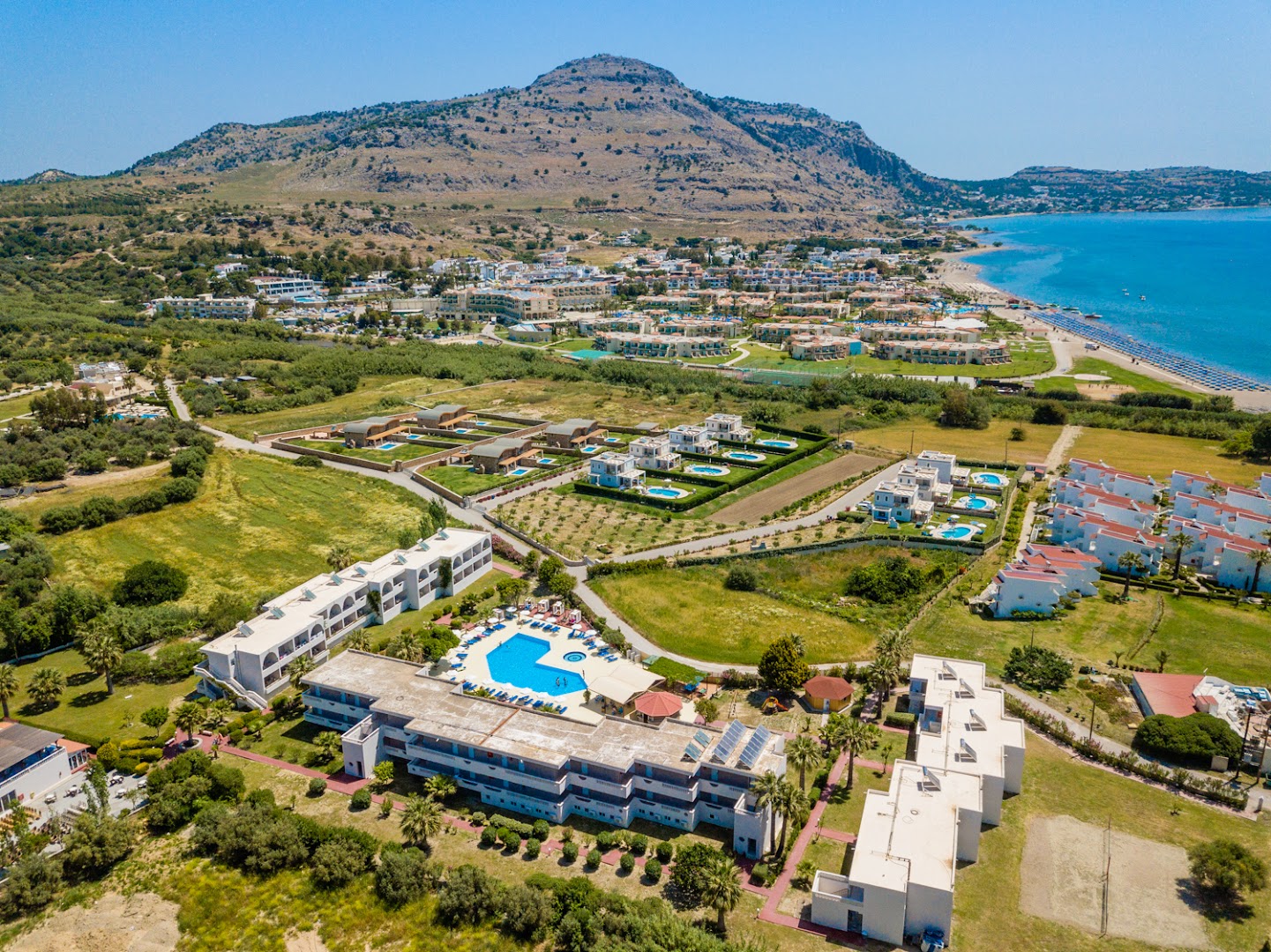 Lardos Bay kompleksa aerofoto ar centrālo baseinu un kalnu fonu Rodas salā — redzami numuru korpusi un apkārtējā infrastruktūra
