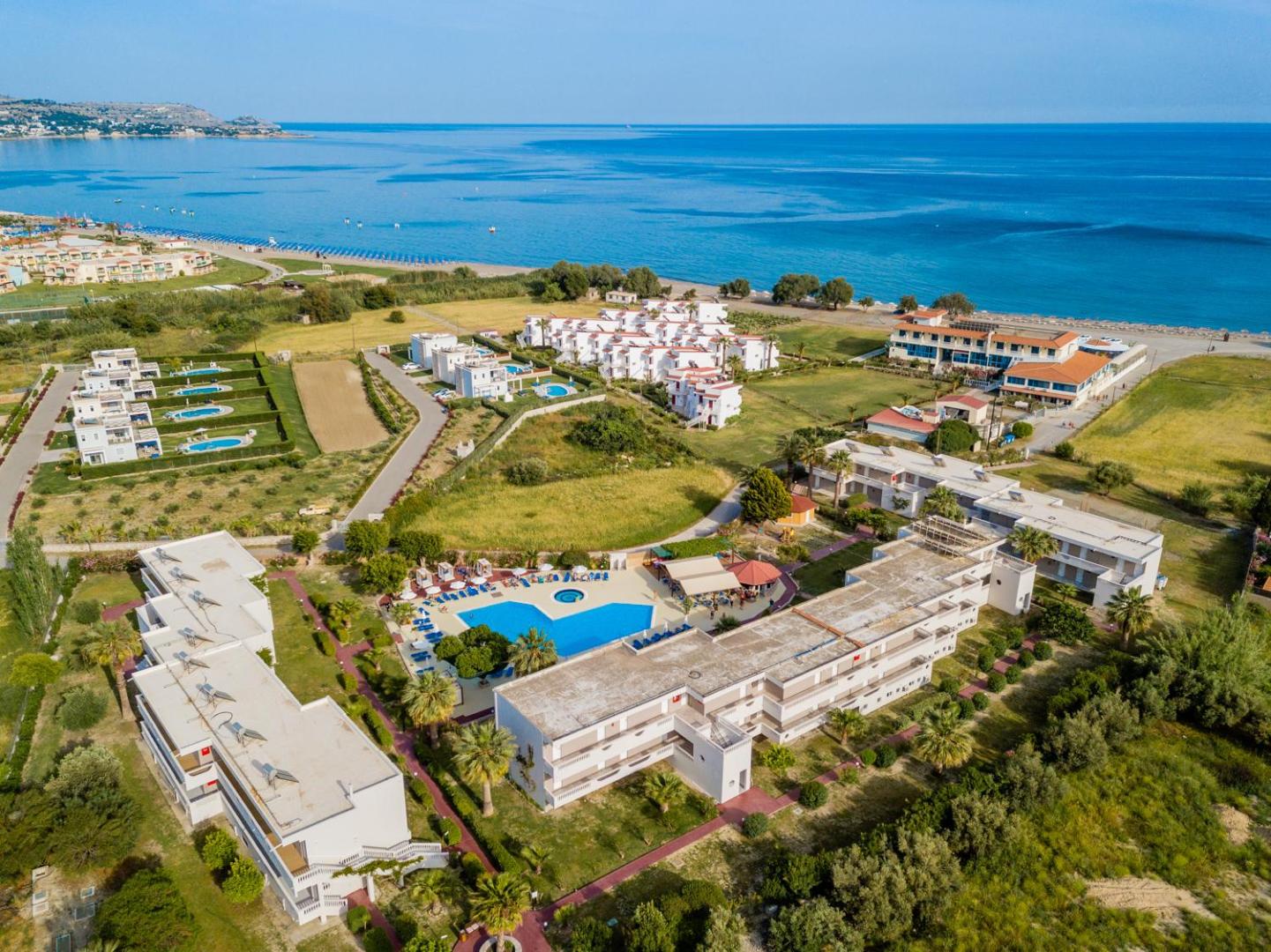 Lardos Bay viesnīcas teritorija ar āra baseinu un numuru korpusiem Rodā — skats uz jūras piekrasti un apkārtējo zaļo zonu