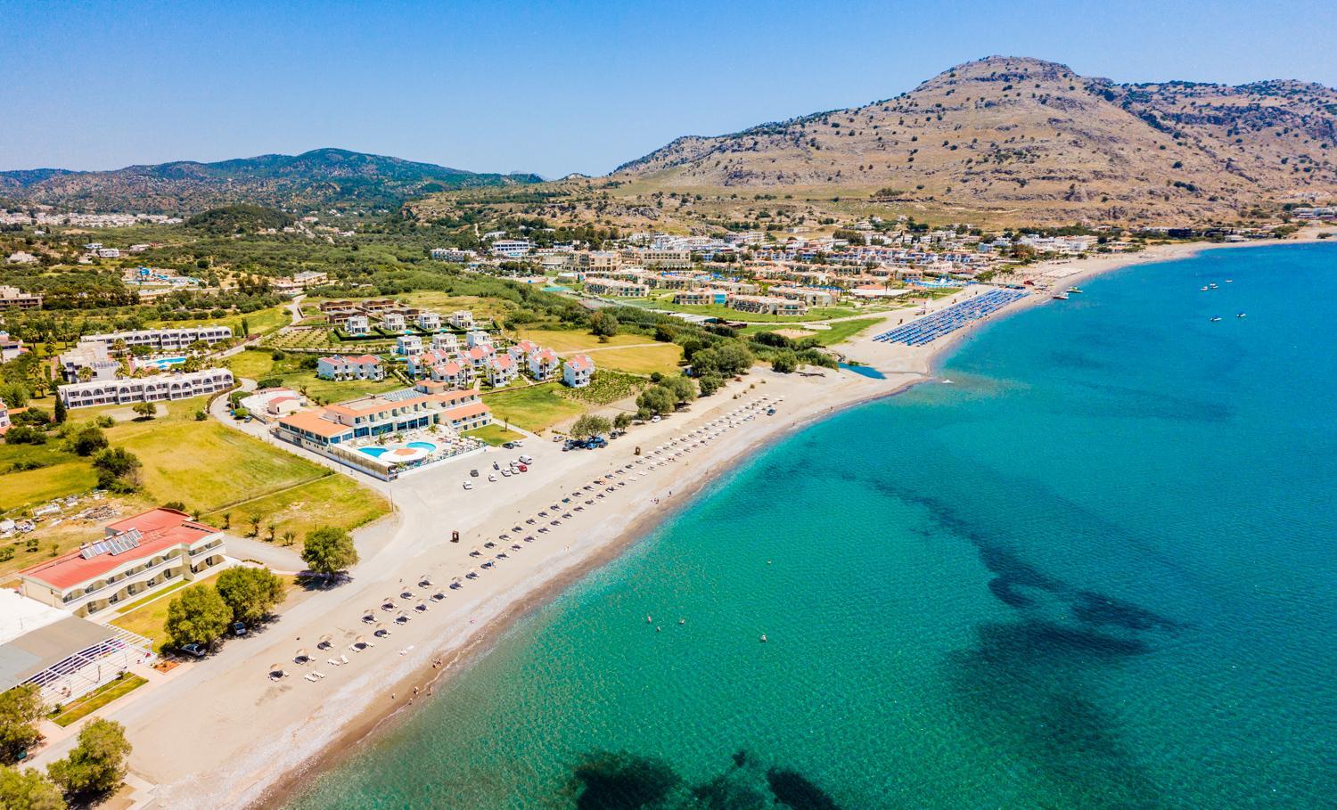 Lardos Bay viesnīcas panorāmas skats no putna lidojuma Rodas salā — plaša smilšu pludmale pie dzidri zilas Egejas jūras un kalnu ainava