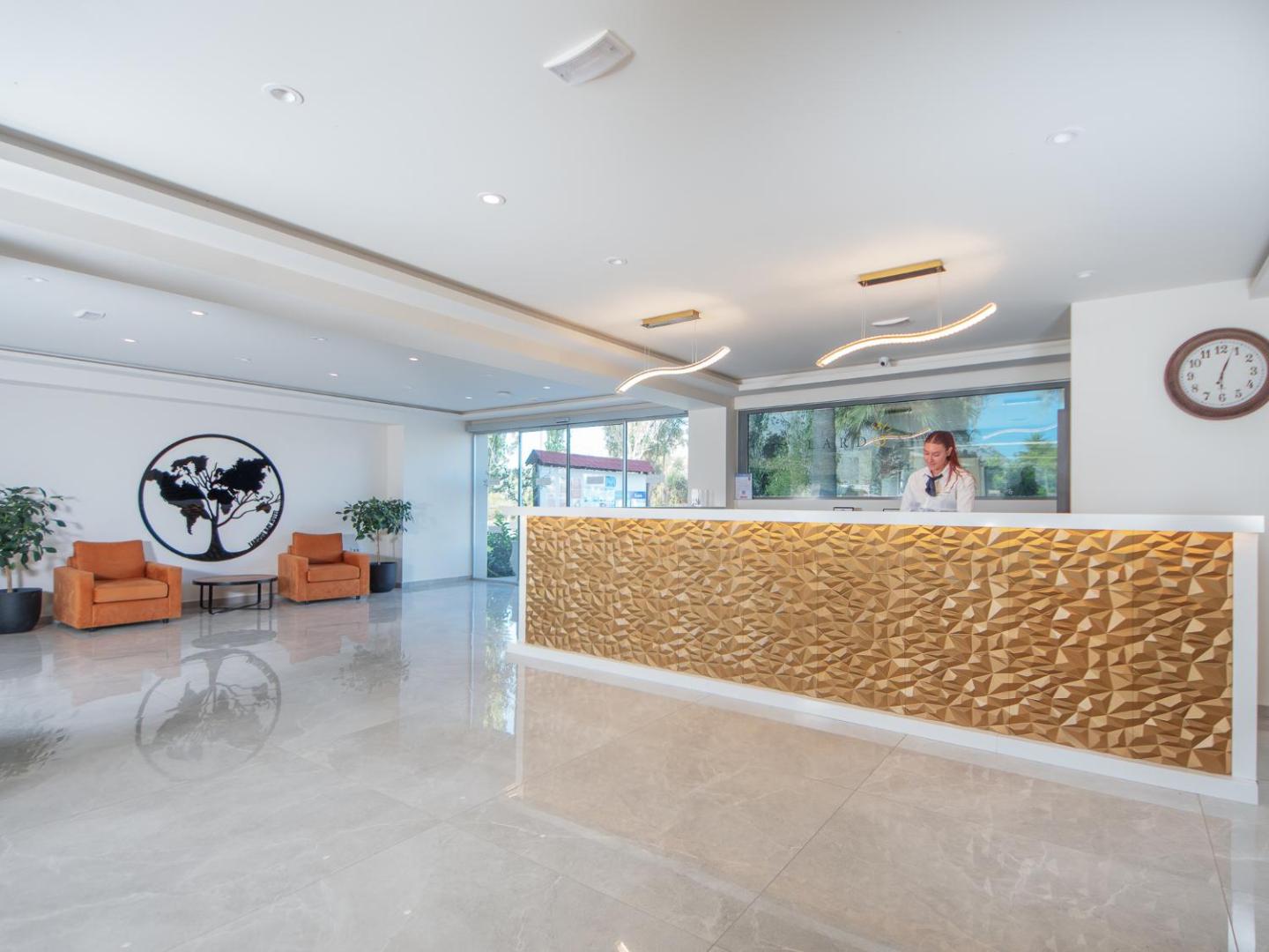 Lardos Bay viesnīcas gaišā recepcijas zona ar modernu zeltītu leti un atpūtas stūri Rodas salā