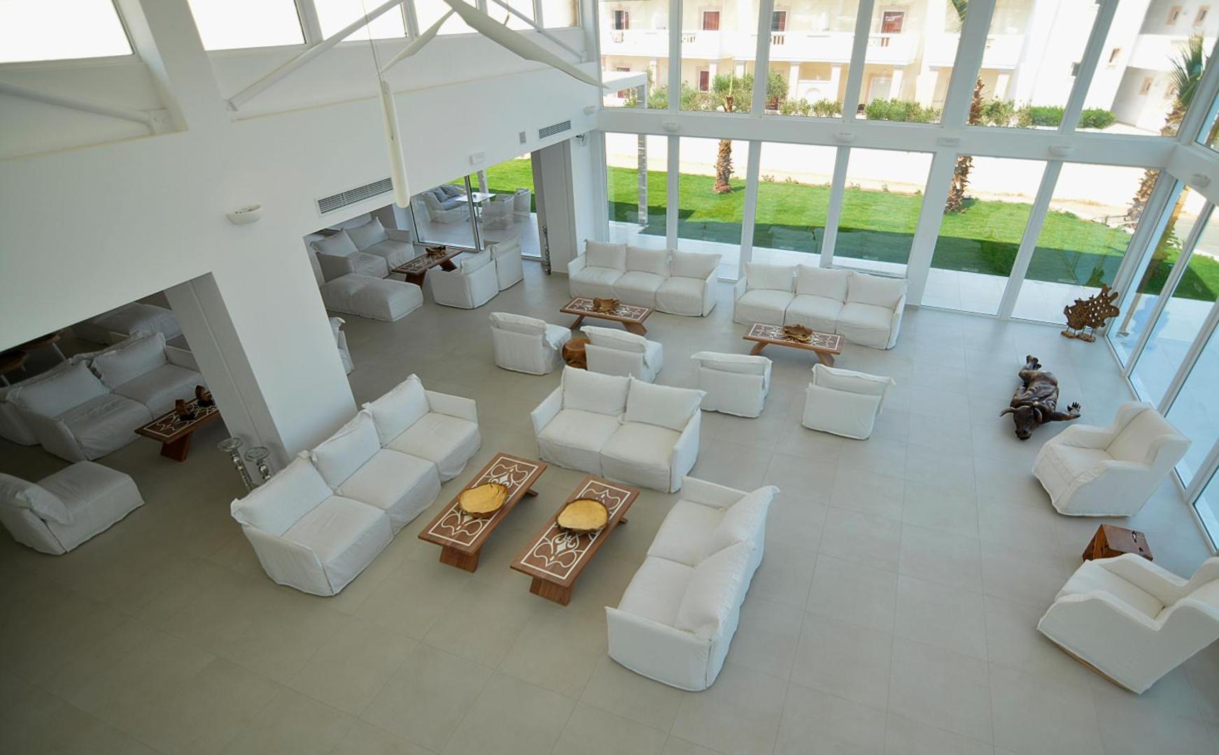 Insula Alba Resort & Spa plašais un gaišais lobby vestibils ar baltiem dīvāniem un lieliem panorāmas logiem uz dārzu