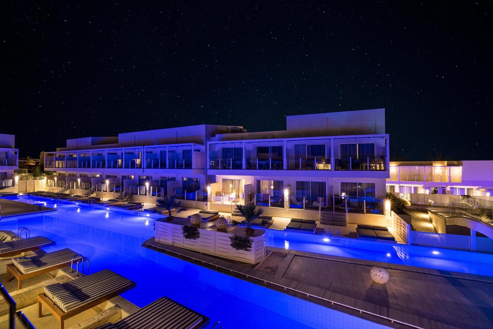 Insula Alba Resort & Spa viesnīcas korpuss un izgaismots baseins naktī zem zvaigžņotām debesīm — moderna arhitektūra un zilas gaismas